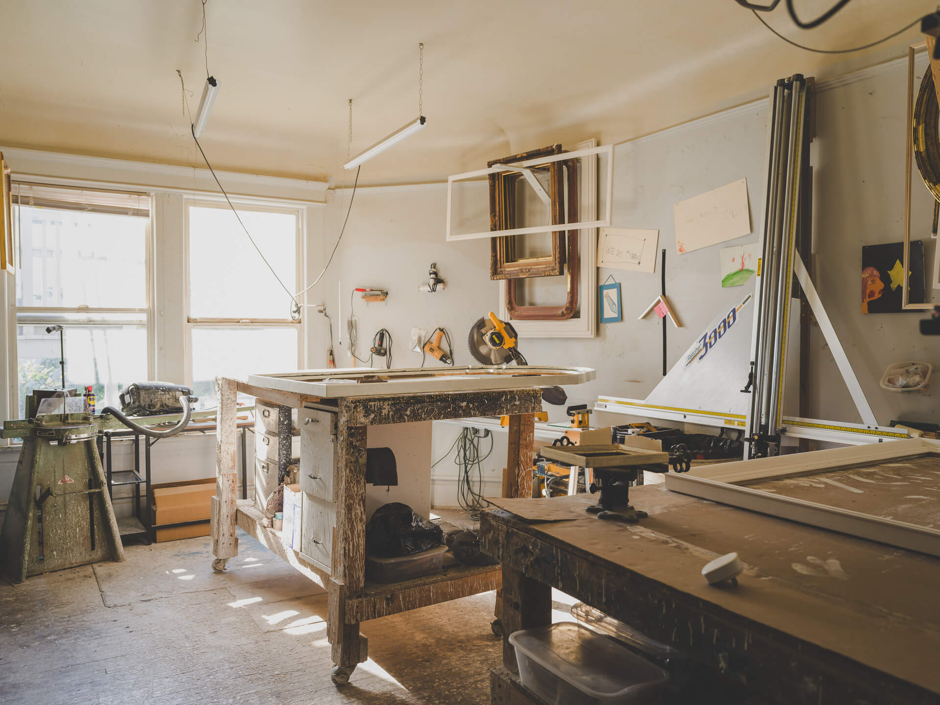 Sunlit workroom at Aedicule with large worktables, framing tools and artwork lining the walls.