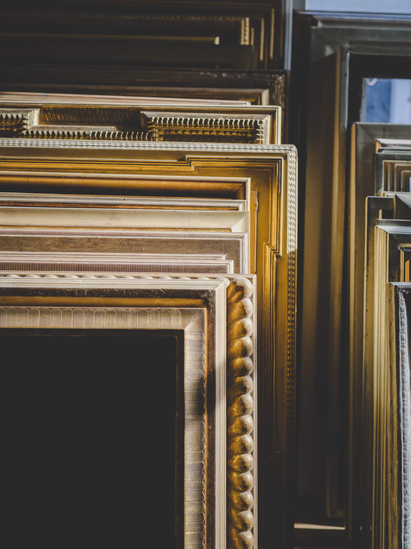 Collection of ornate gold and black picture frames stacked vertically inside the Aedicule workshop.