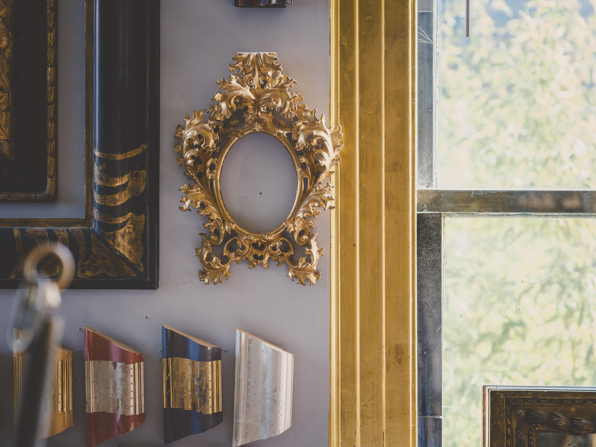 Detail of an ornate gilded frame and decorative objects beside a sunlit studio window.