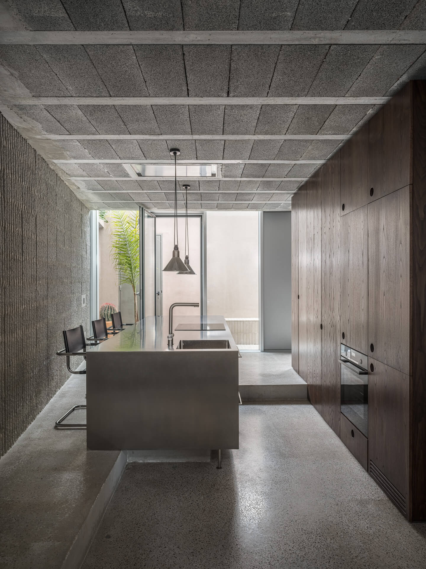 Minimal kitchen with stainless steel island, dark wood cabinetry, and an exposed concrete ceiling