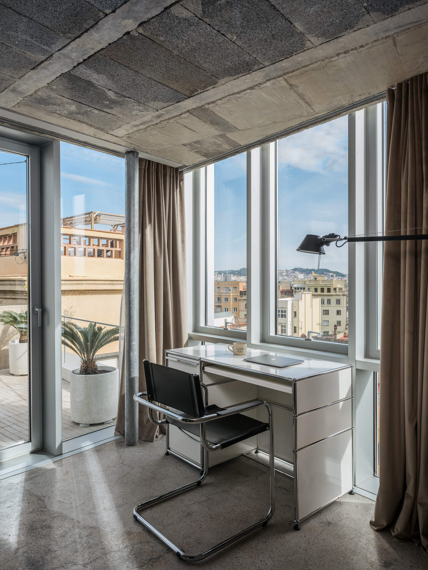 Compact desk and chair positioned beside corner windows with city views.