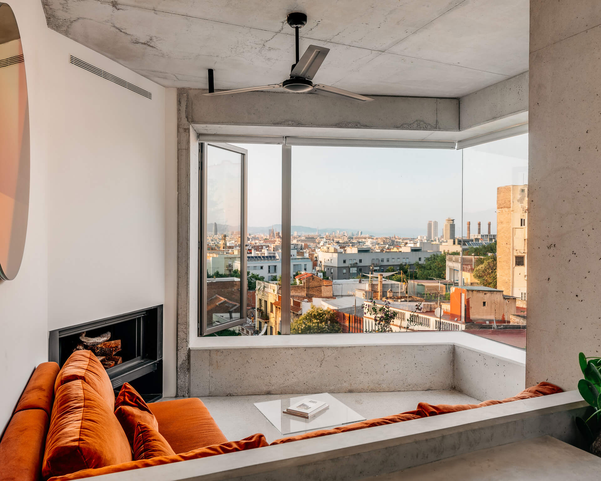 Concrete living room with rust-colored sofa, corner windows, and expansive city views.