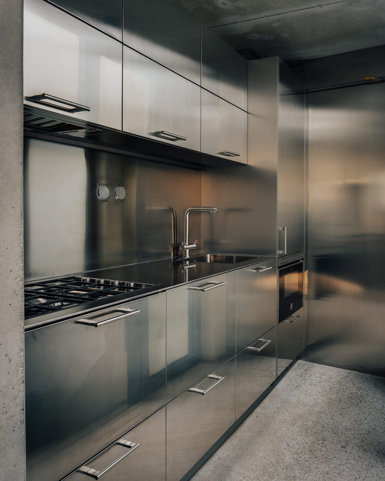 Minimal galley kitchen with stainless steel cabinetry, countertops, appliances, and backsplash.