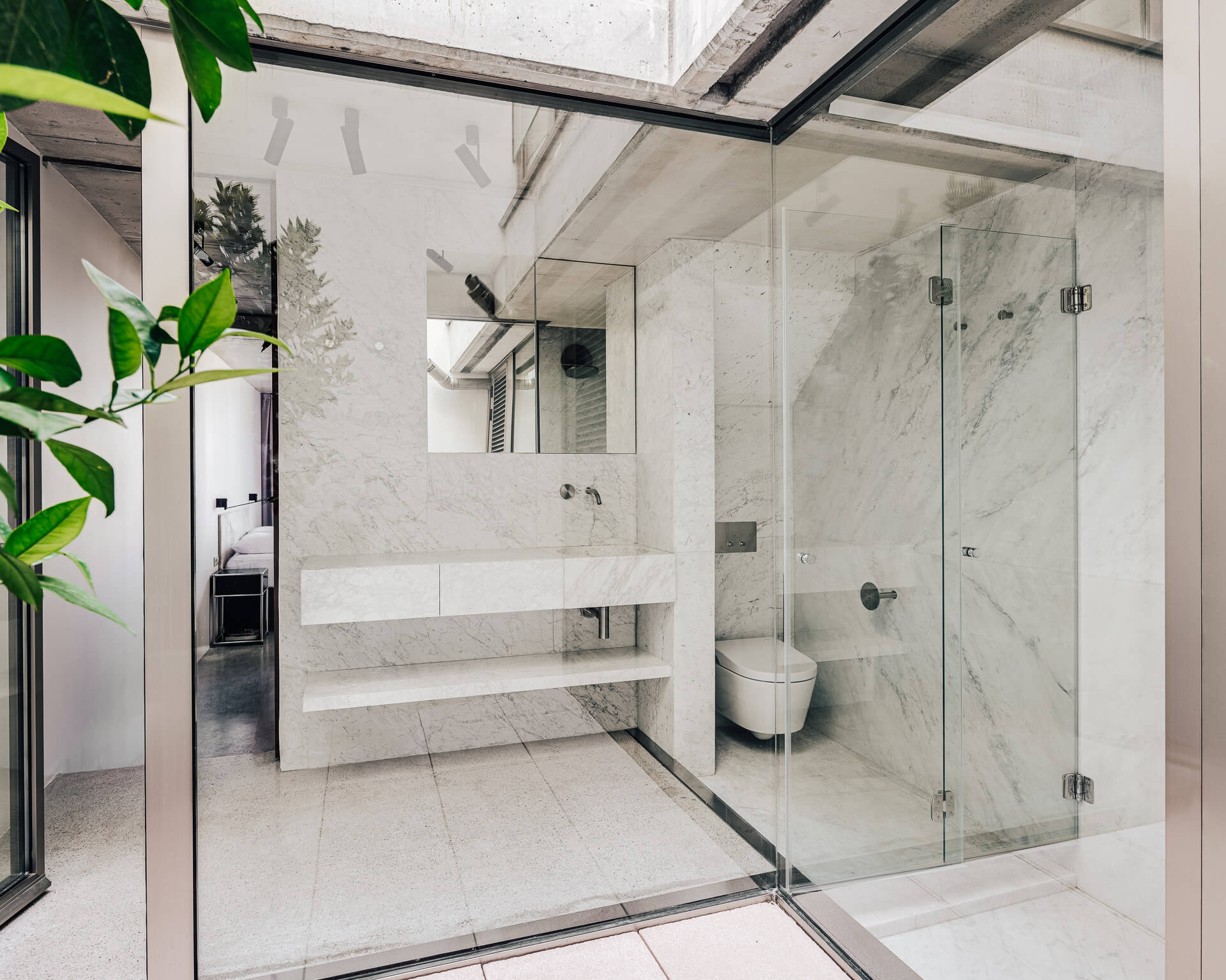 Bright bathroom with glass-enclosed shower, white surfaces, built-in bench, and overhead skylight.