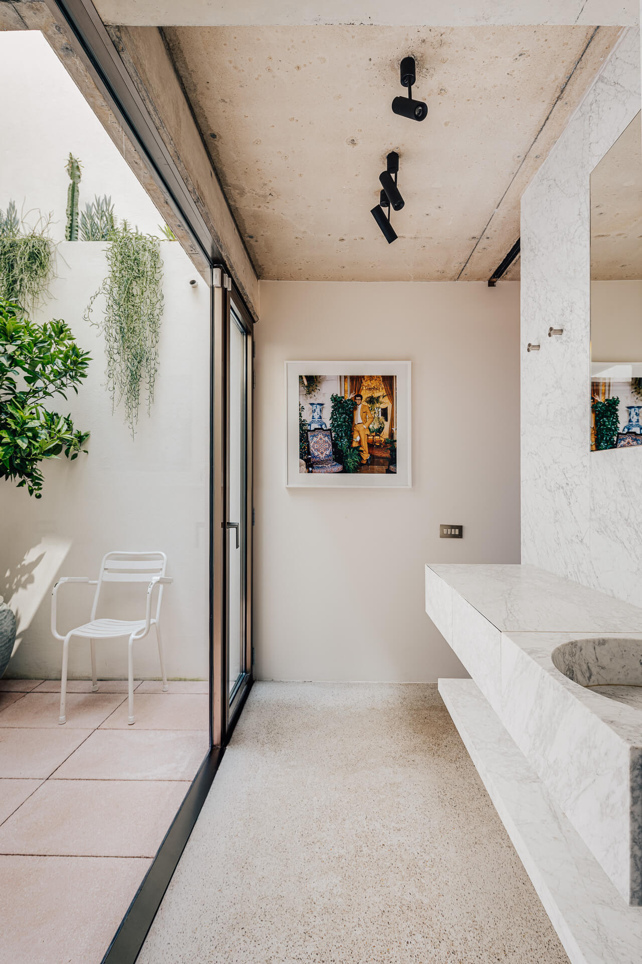 Long, narrow bathroom and terrace with concrete walls, seating, plants, and large sliding glass doors.