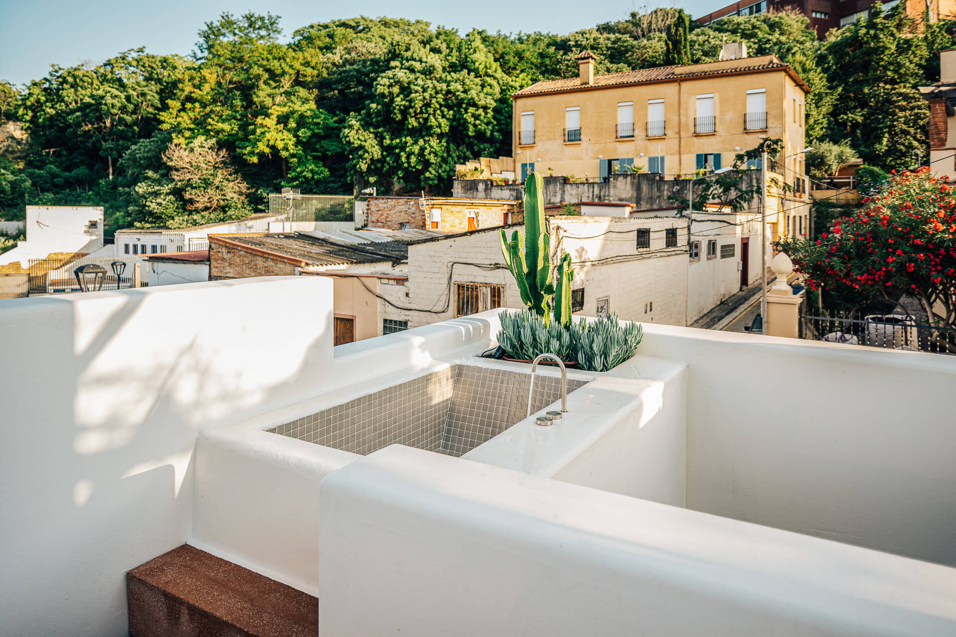 White rooftop terrace with a small plunge pool surrounded by neighboring hillside homes
