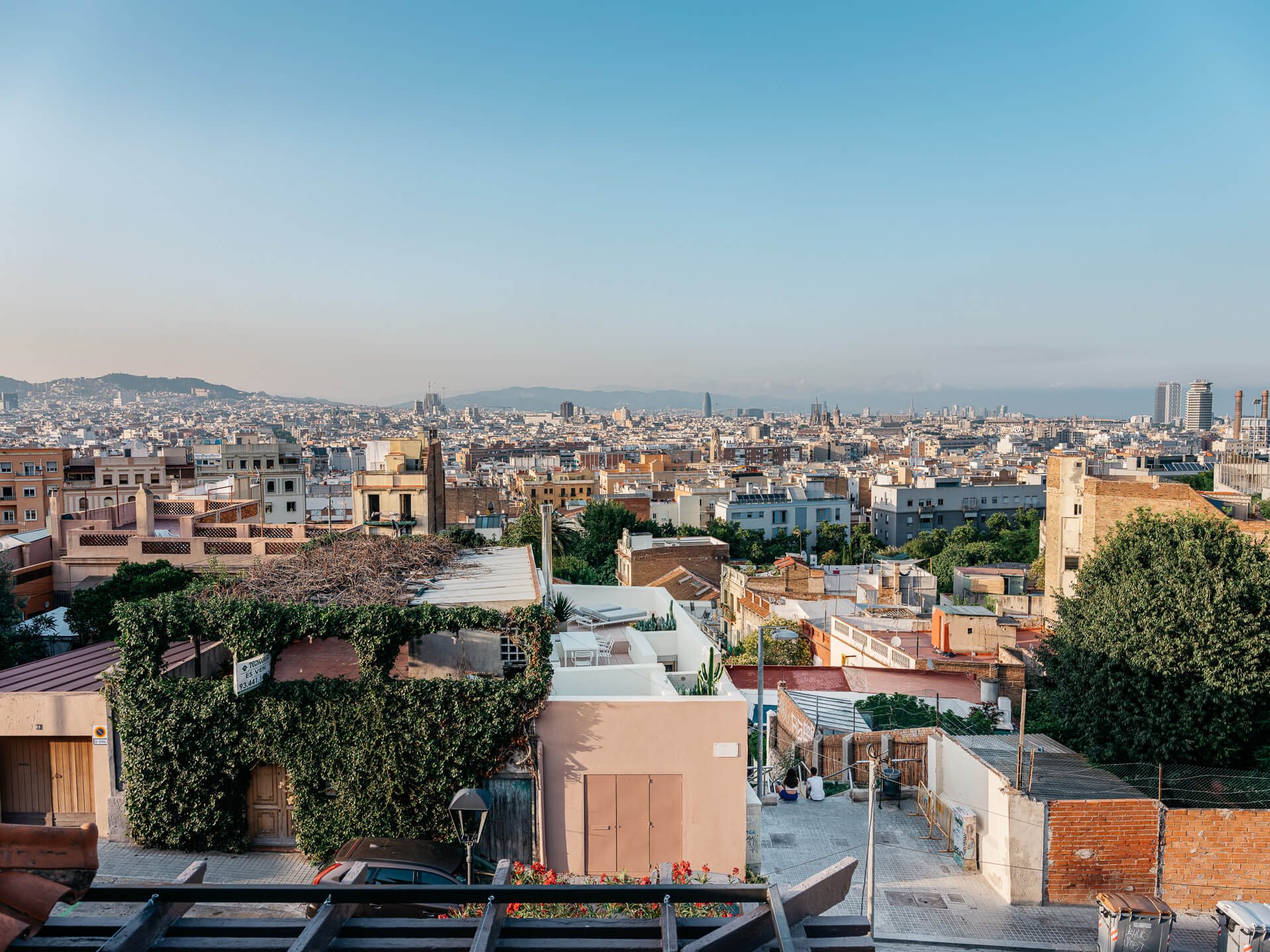 Panoramic view over city rooftops toward distant hills and the skyline beneath a clear blue sky