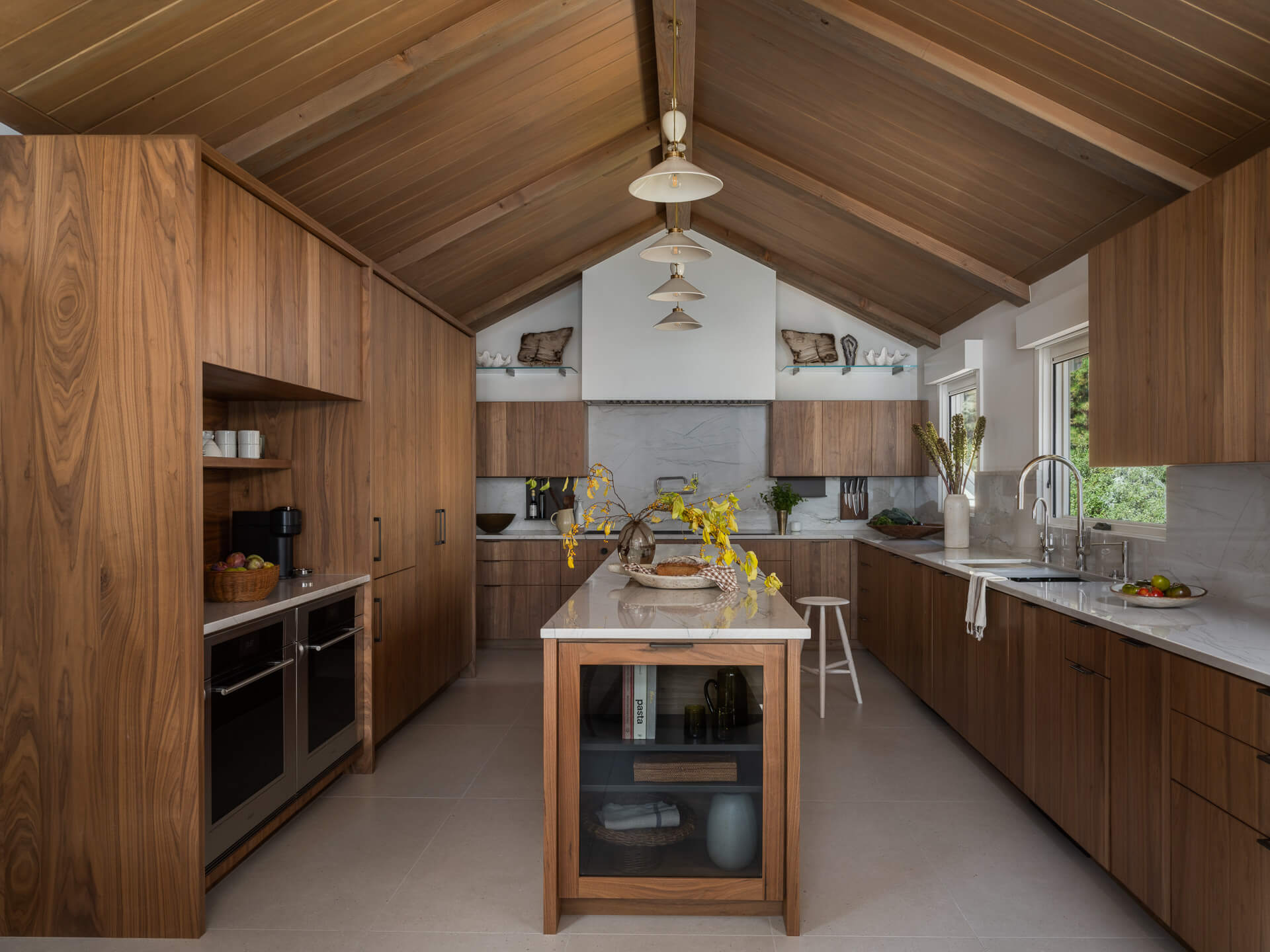 Warm wood-paneled kitchen with vaulted ceiling, central island and minimalist white pendant lights.
