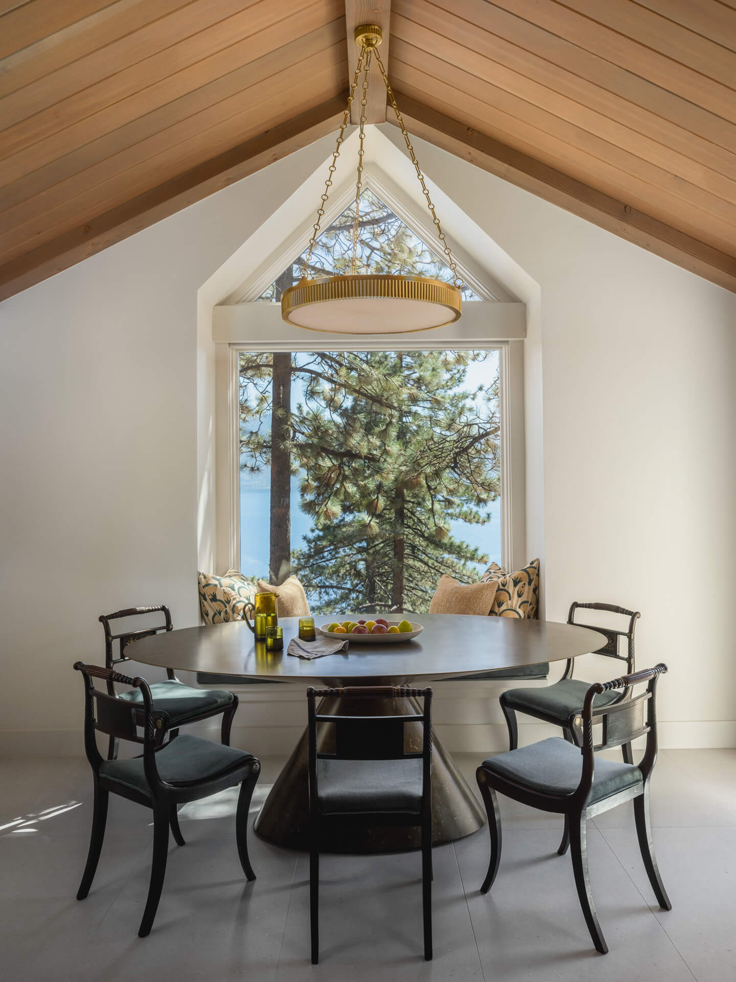 Dining nook beneath a peaked wood ceiling with sculptural chandelier and framed view of the surrounding pines.