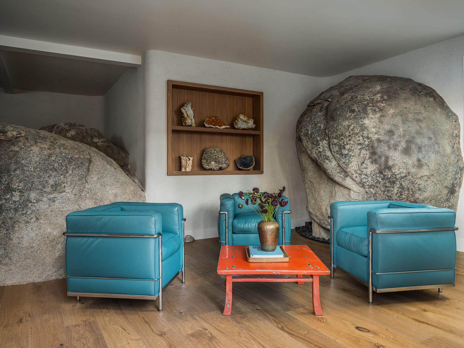 Sitting area built around natural granite boulders with bright blue lounge chairs and a red coffee table.