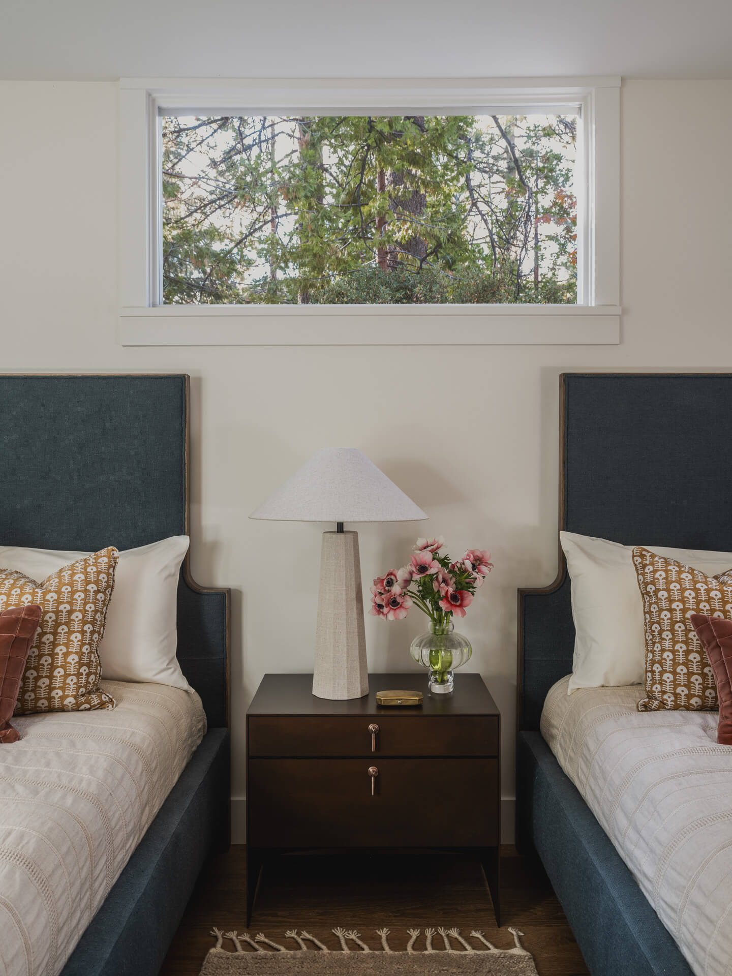 Symmetrical twin bedroom with upholstered blue headboards, central nightstand and forest view.