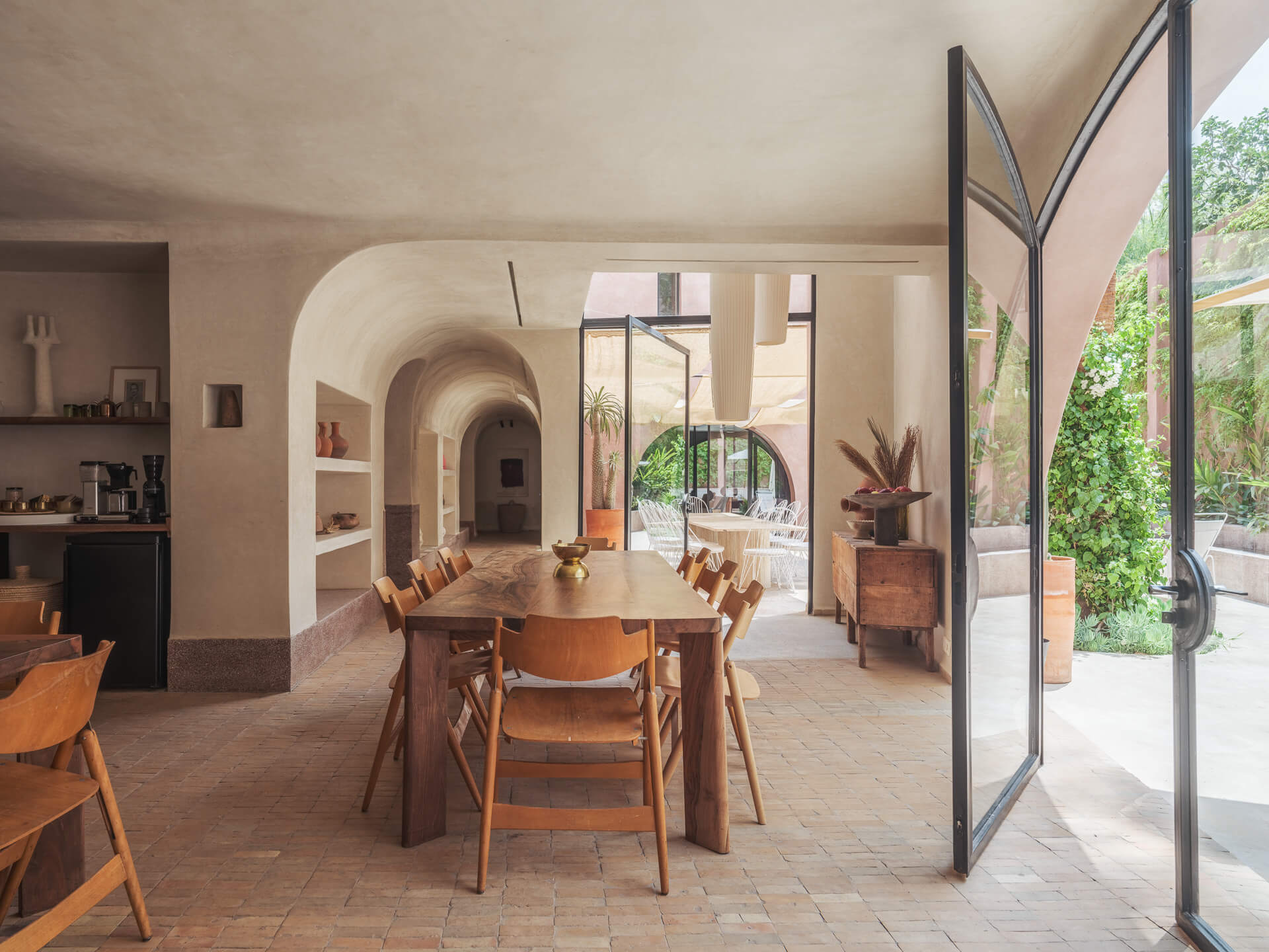 Open dining room with wood table and chairs, arched doorways, and glass doors opening to the courtyard.
