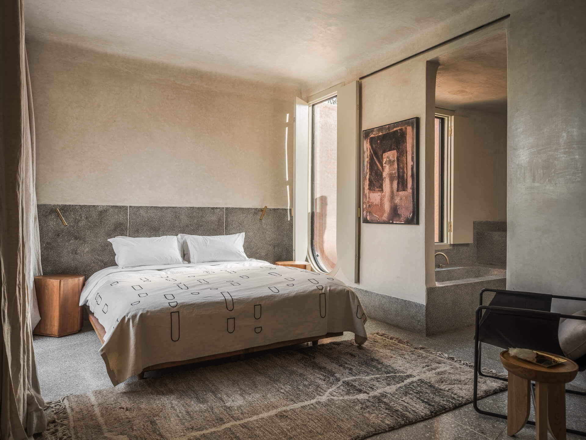 Serene bedroom with low bed, textured plaster walls, framed artwork, and a dark lounge chair.