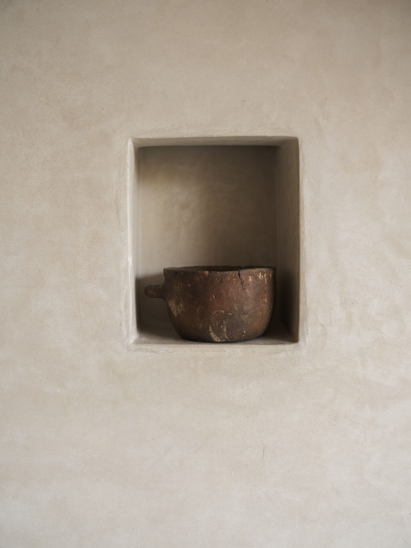 Small rustic vessel displayed in a recessed niche in a pale plaster wall.