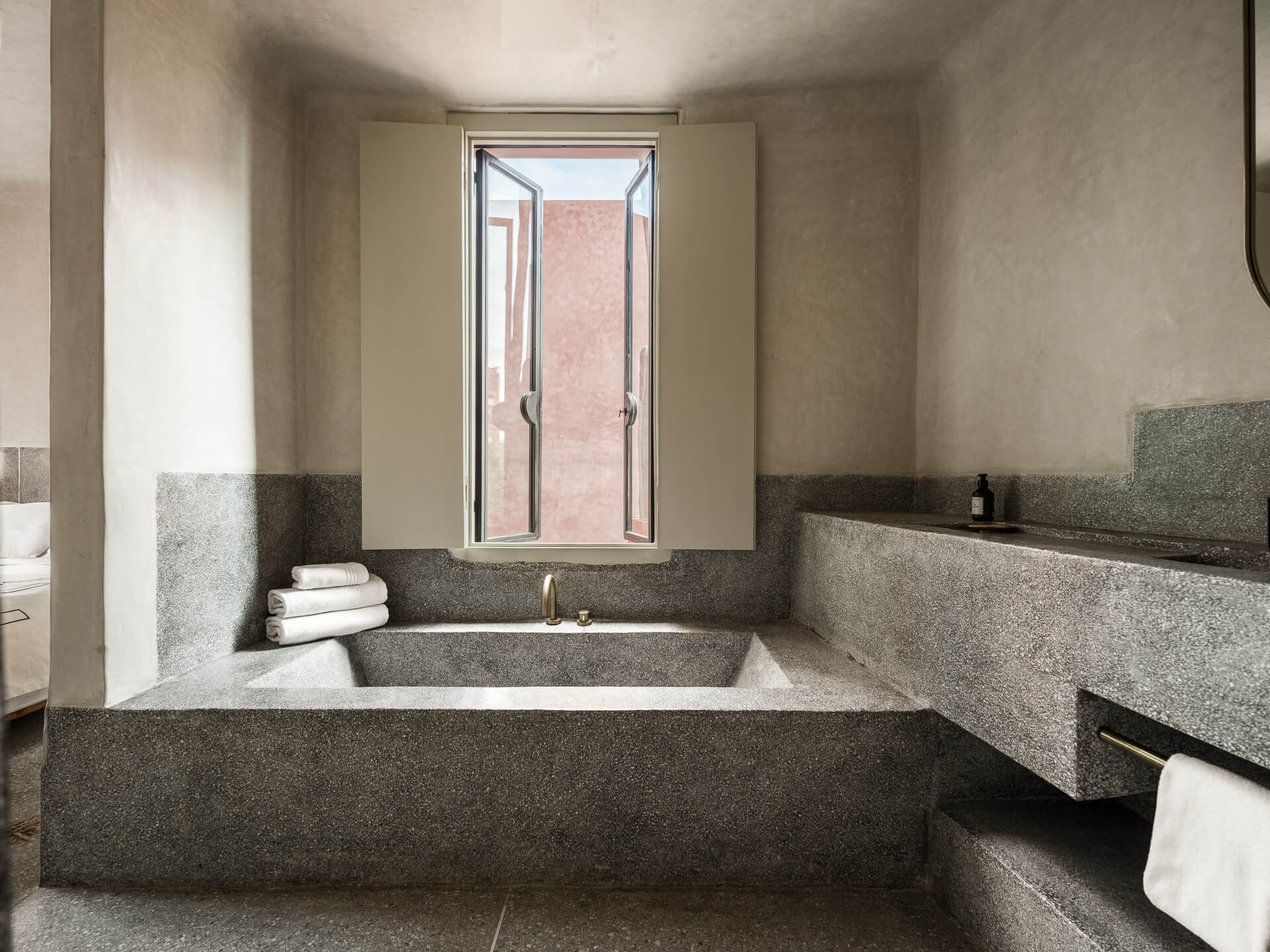 Built-in stone bathtub beneath a narrow window with folded white towels nearby