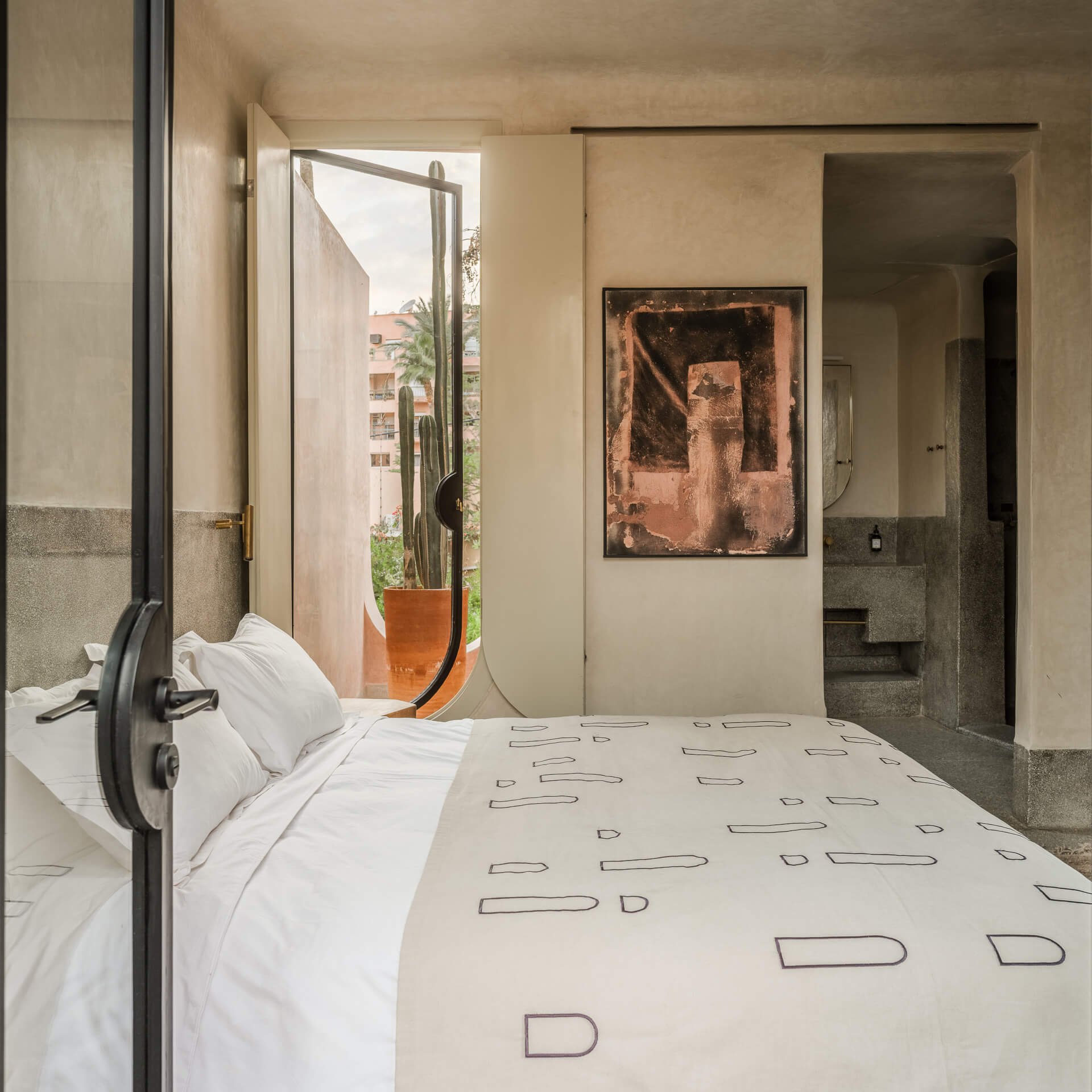 Bedroom with patterned white bedding, framed artwork, and an open doorway leading to the bath.