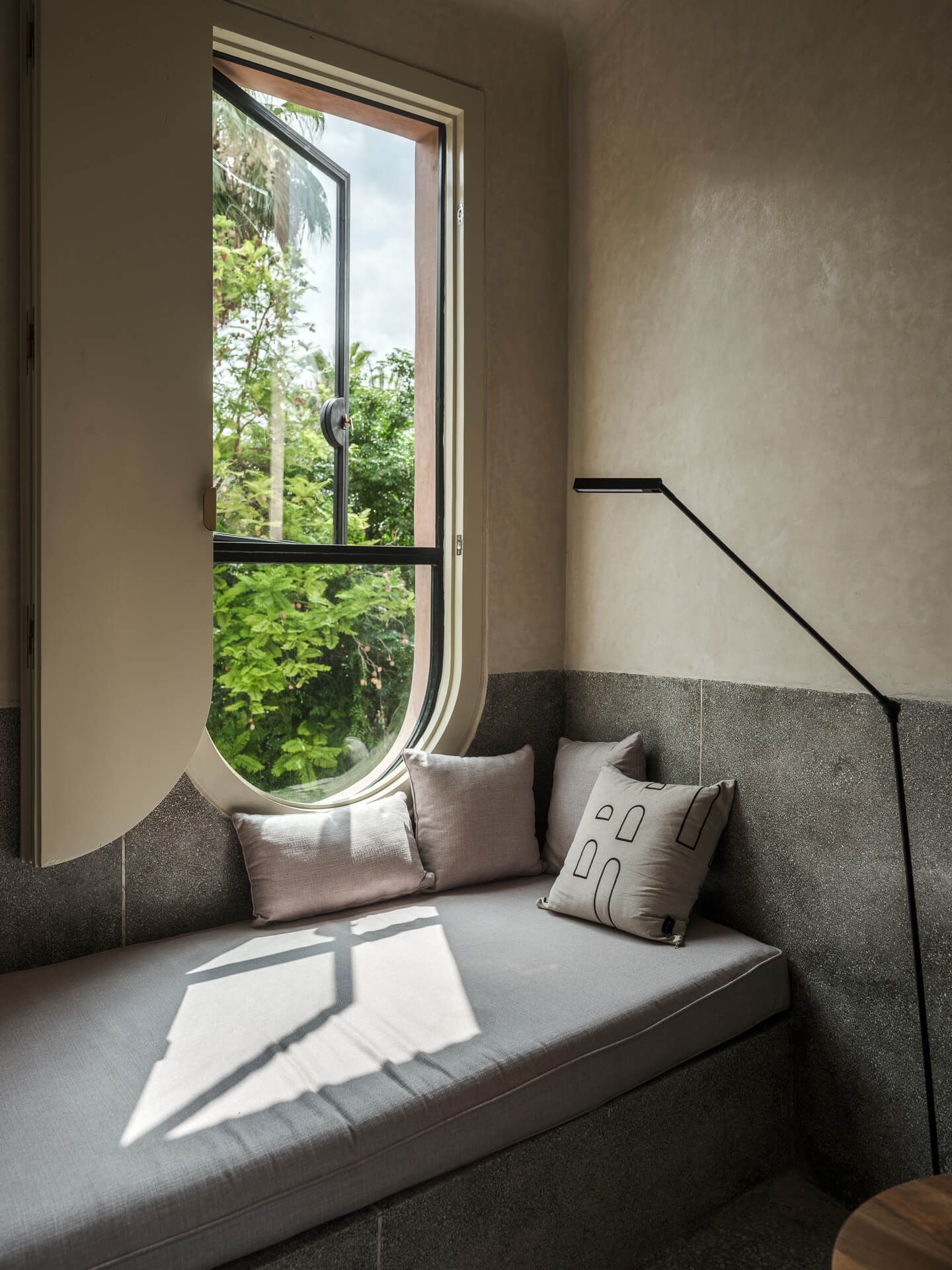 Built-in window seat beneath a tall curved window overlooking lush greenery.