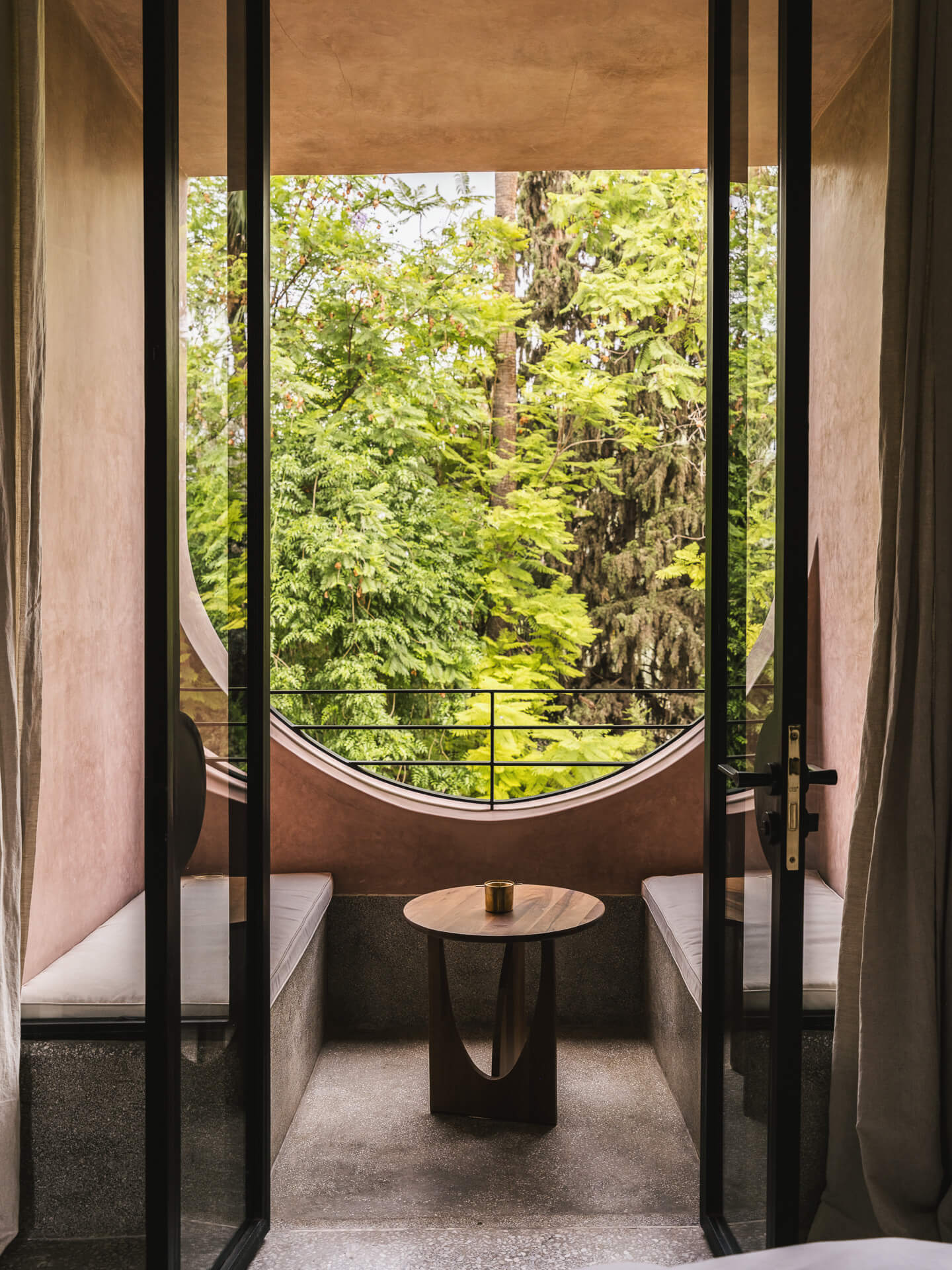 Intimate window nook with a curved opening and small round table overlooking dense green foliage.