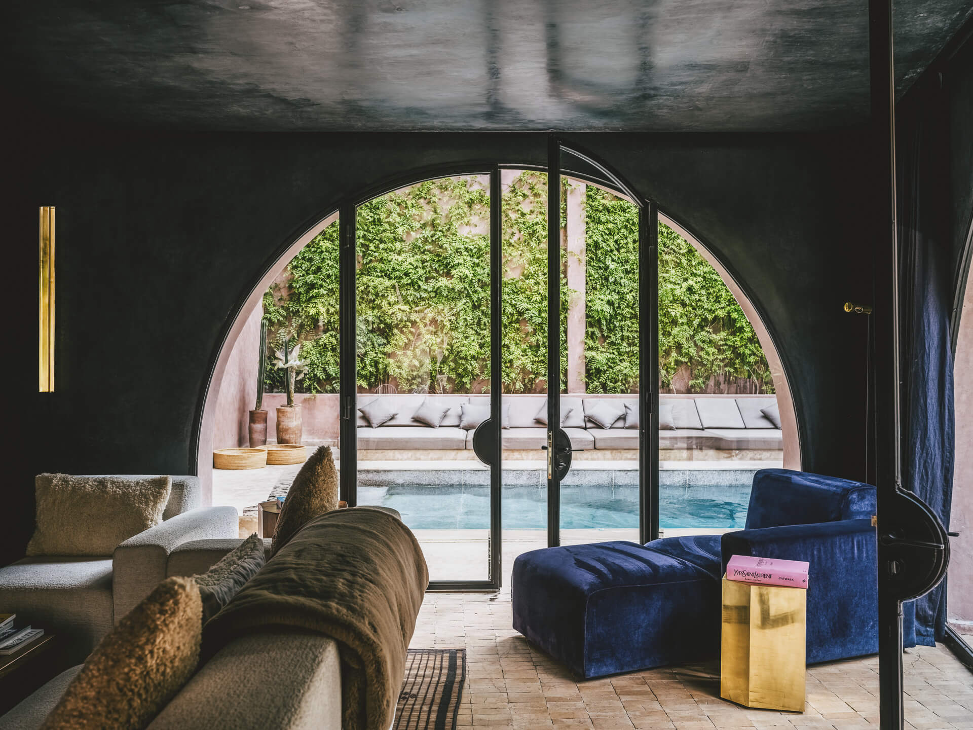 Dark living room opening through a large arched glass doorway to the pool and garden.