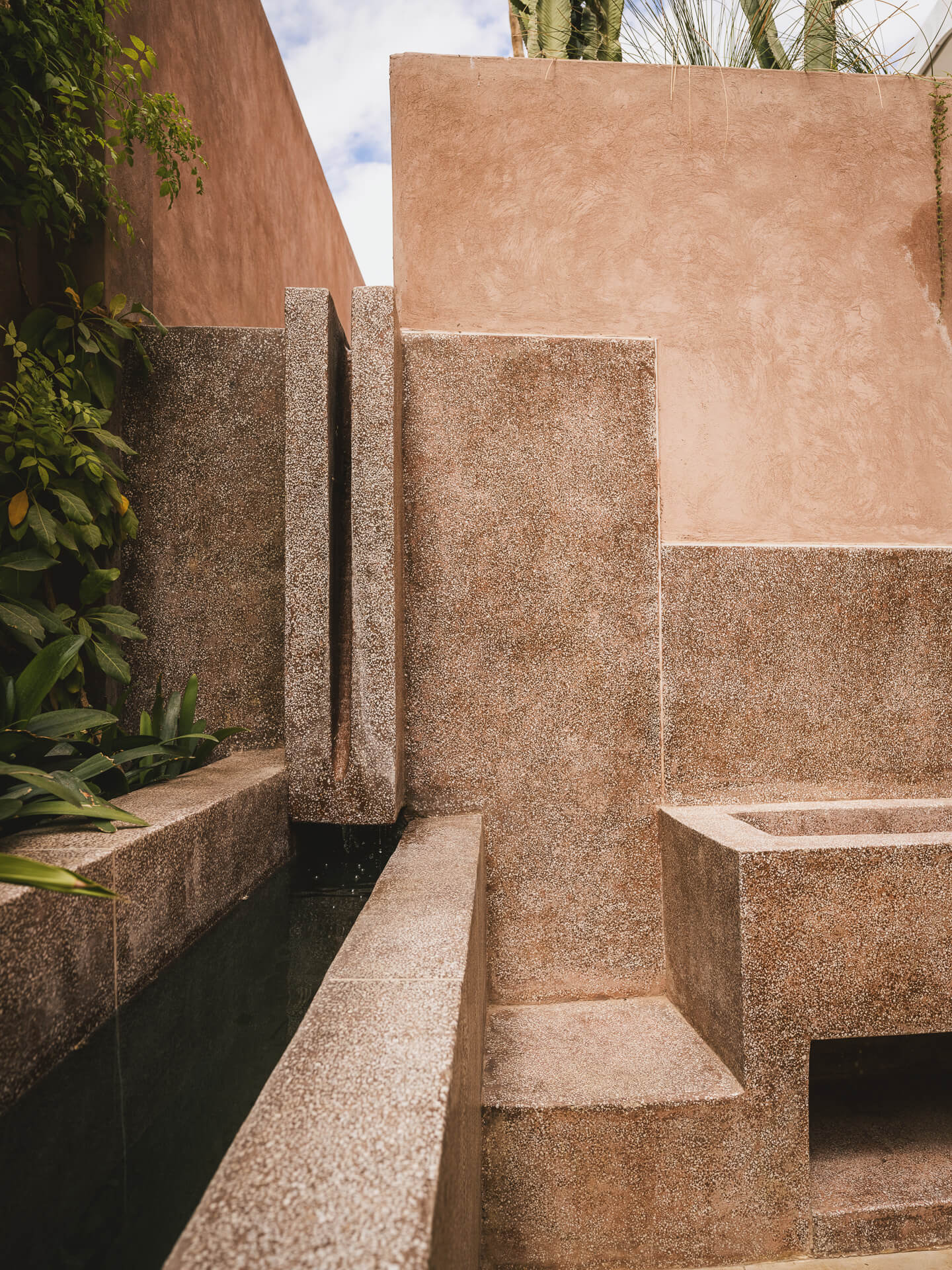 Geometric stone steps and walls beside a narrow water channel in a pink-walled courtyard.