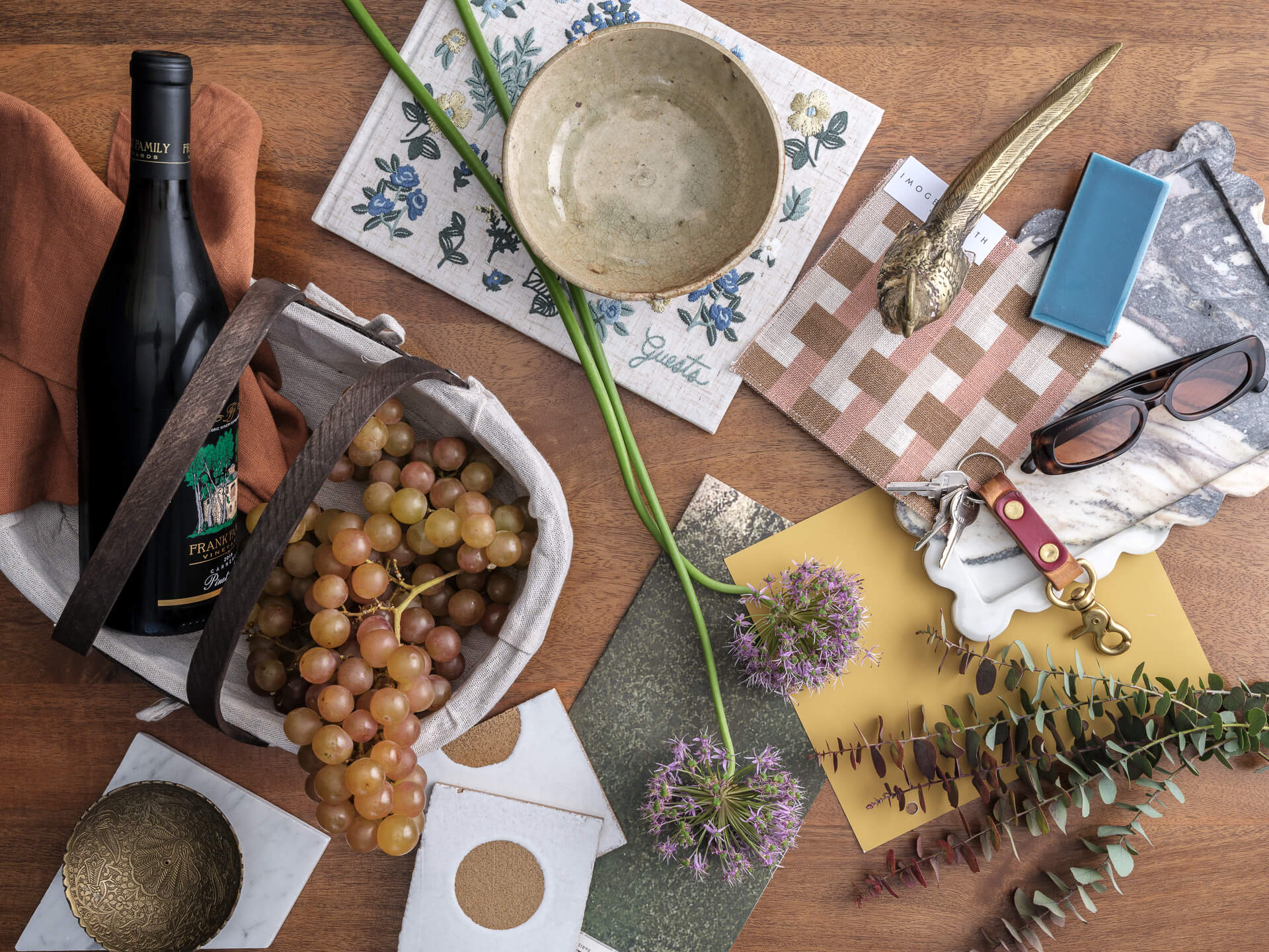 Overhead composition with wine bottle, grapes, tile and fabric samples, ceramics and botanical elements