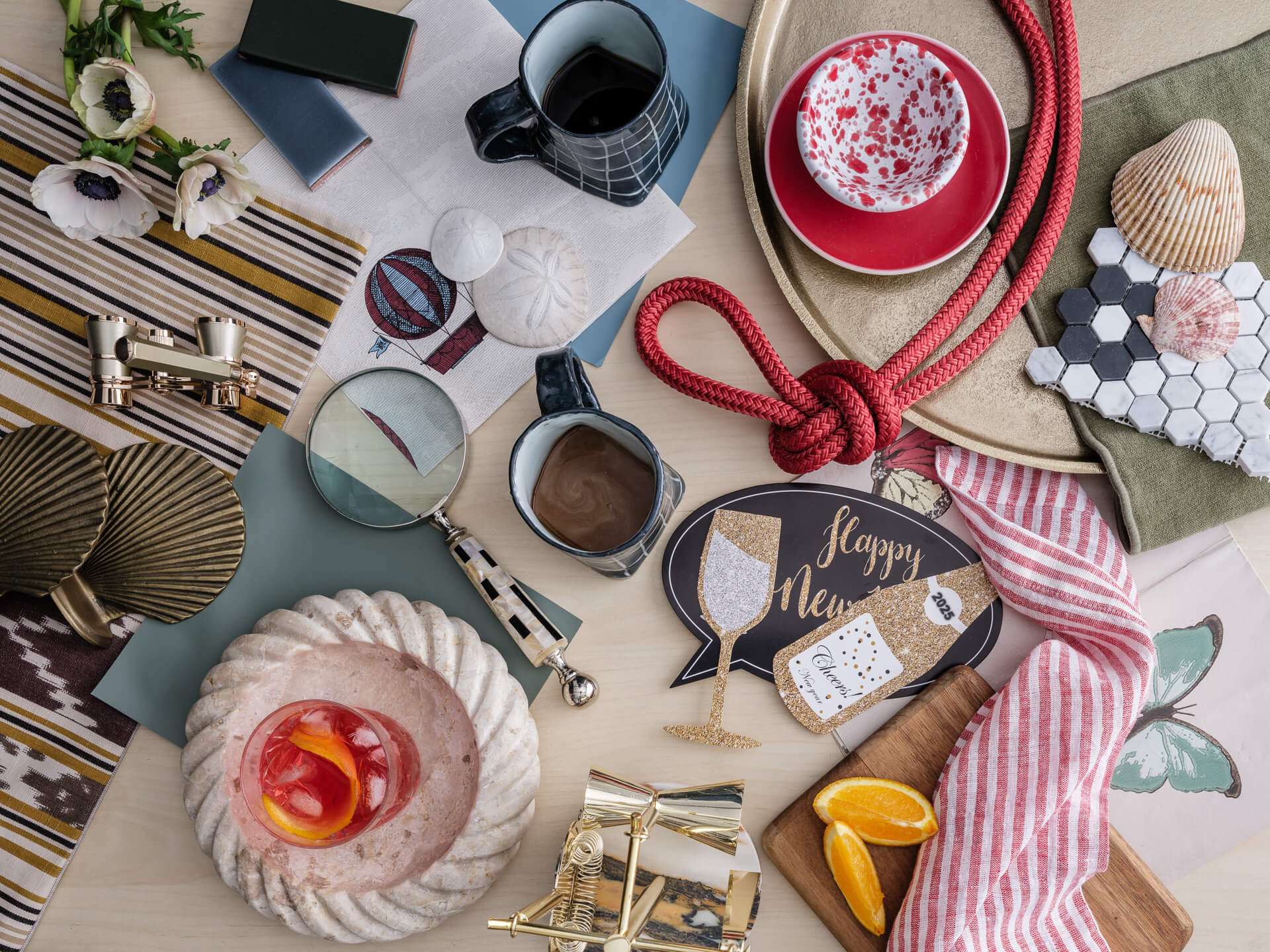 Graphic overhead arrangement of red glassware, striped textiles, ceramics, fabric samples and small design objects