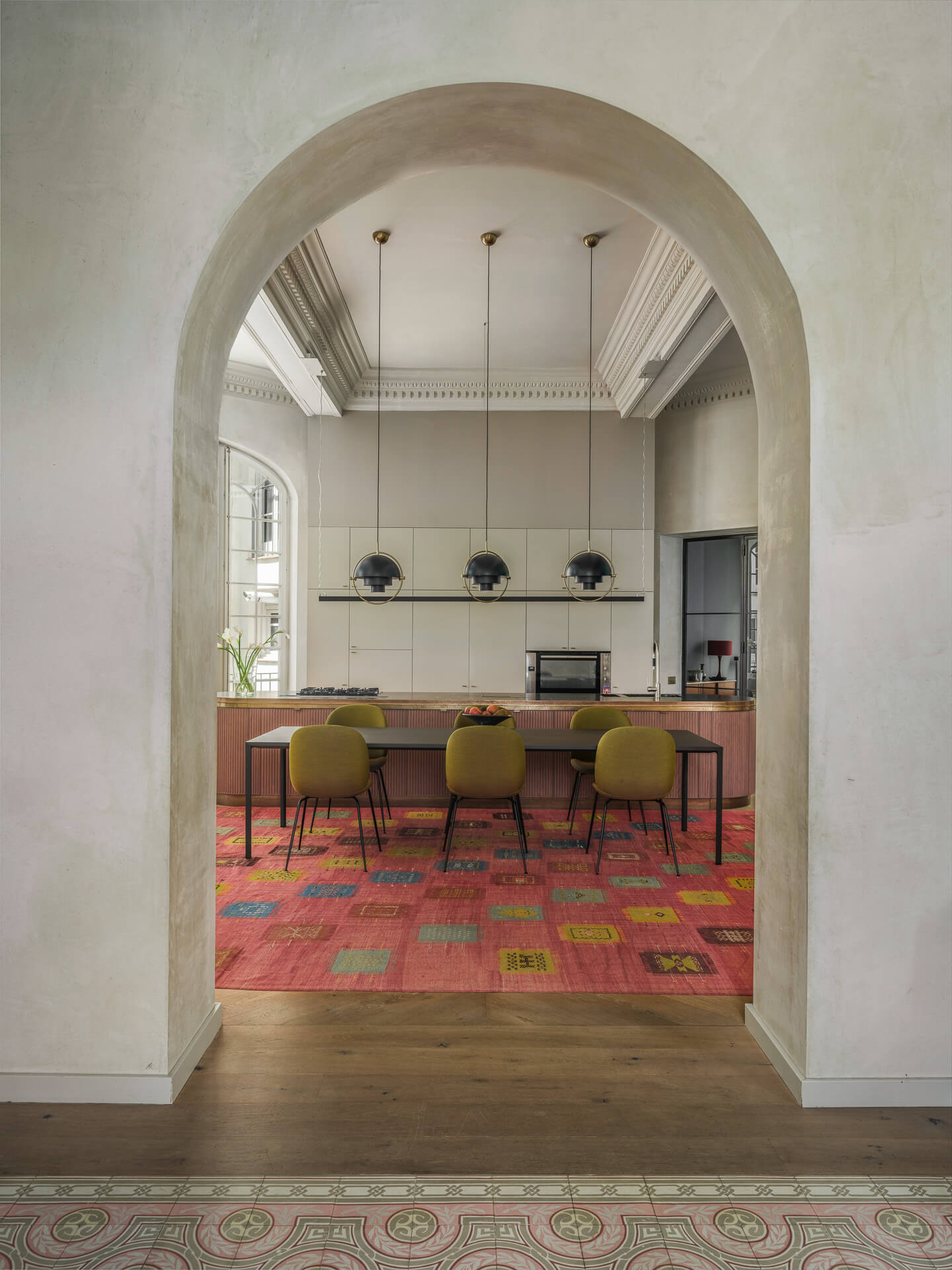 Large arched doorway framing a dining room with colorful rug, green chairs, and pendant lights.