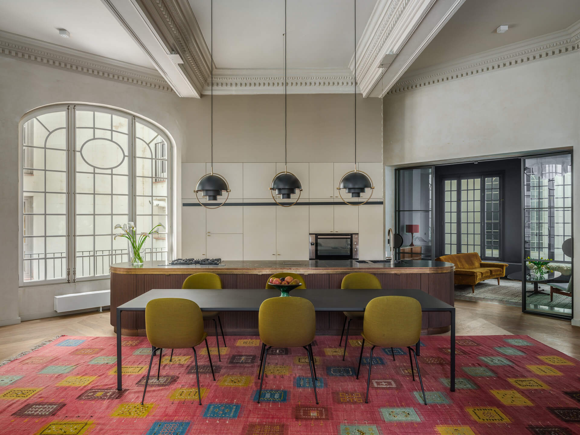 Spacious dining room with long wood table, green chairs, colorful geometric rug, and tall arched windows.