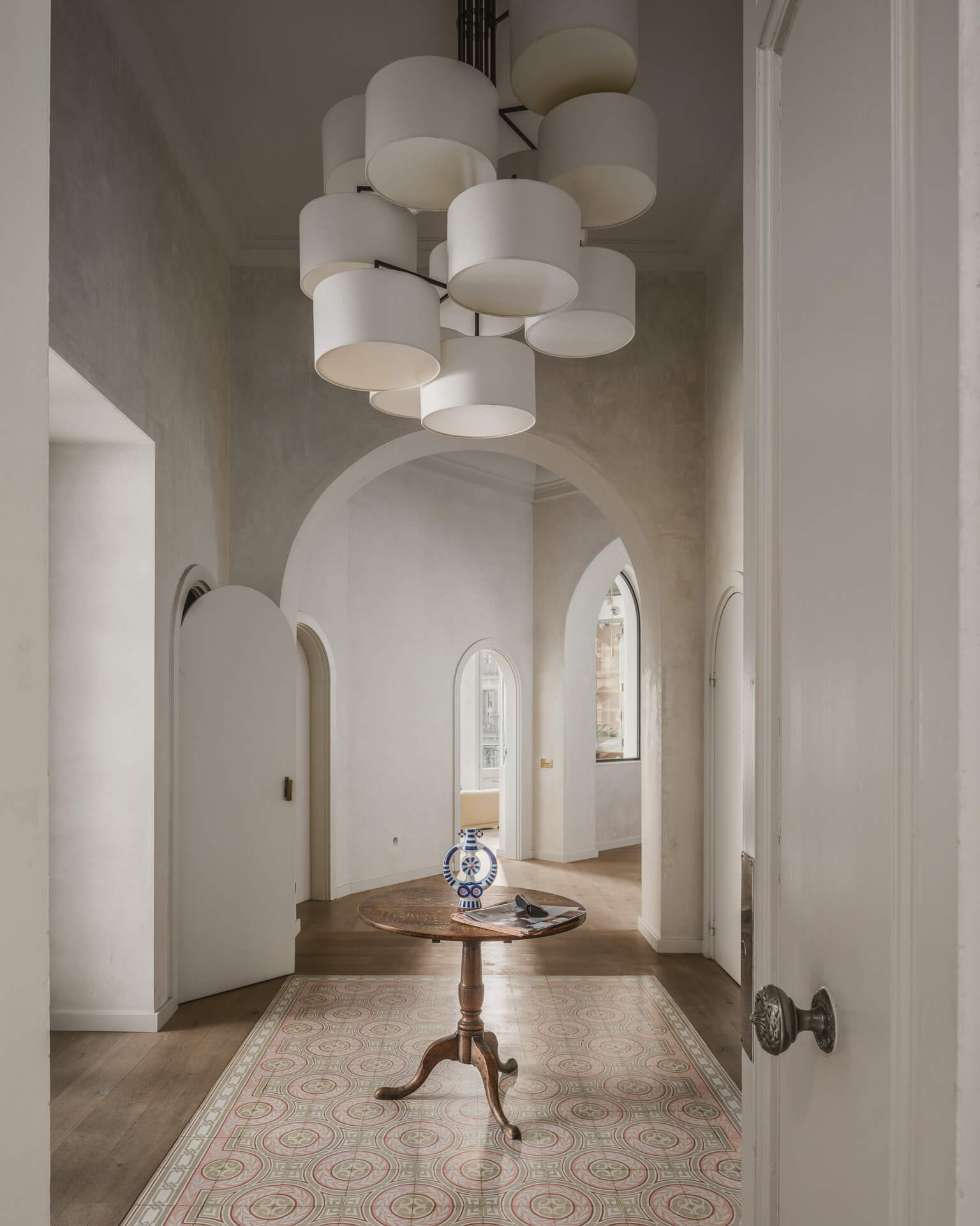 Pale arched hallway with clustered white pendant lights, patterned runner, and a small round table.
