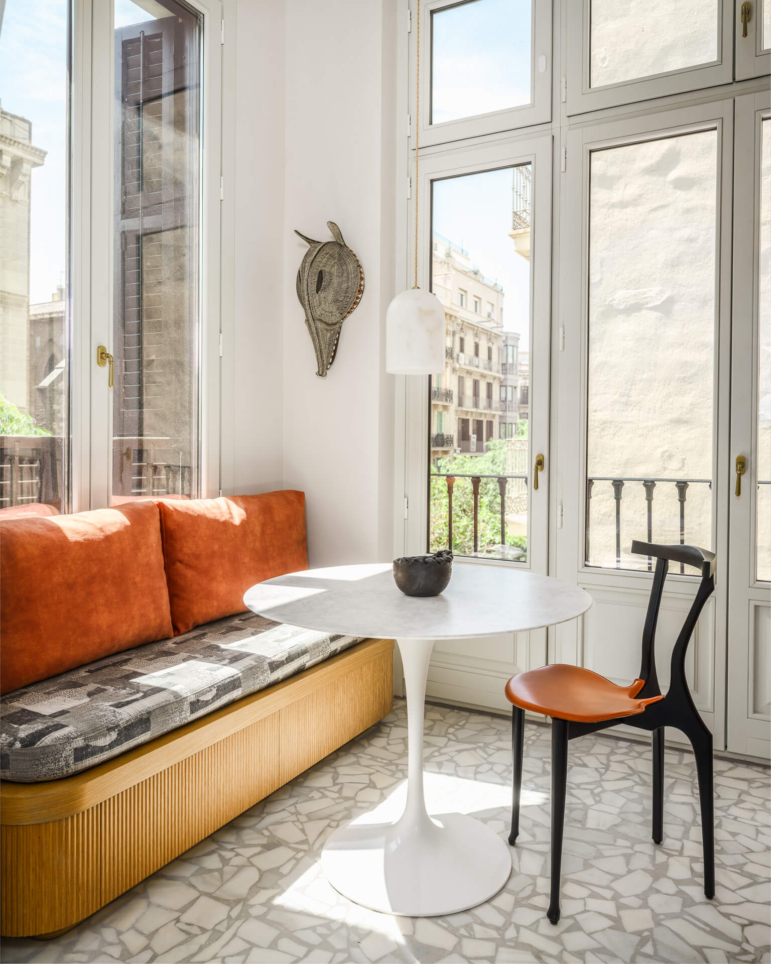 Sunlit breakfast nook with built-in orange bench, round white table, black chairs, and tall windows.