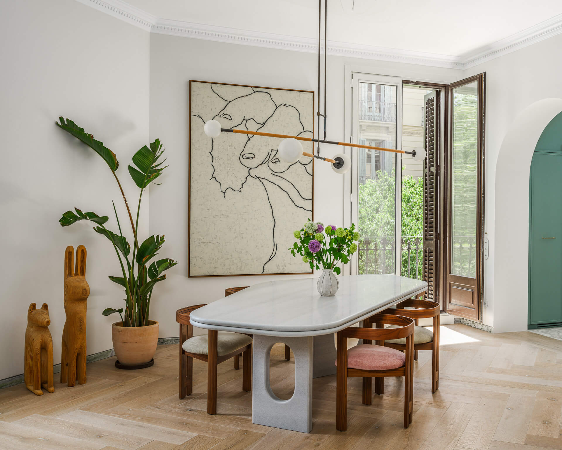 Dining room with oval stone table, wood chairs, large artwork, potted plant, and sculptural pendant light.