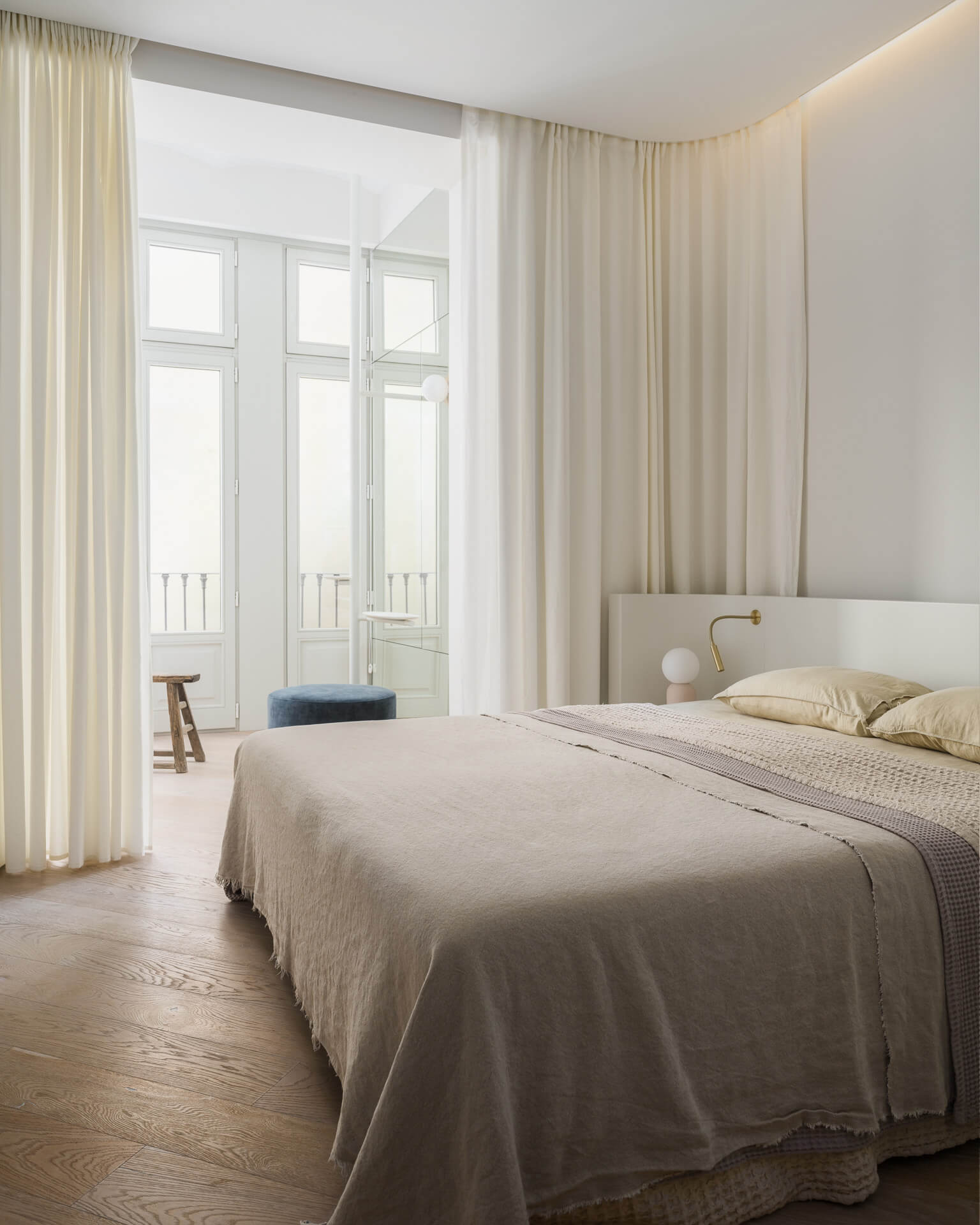Serene bedroom with neutral bedding, full-height curtains, and tall French doors opening to a balcony.