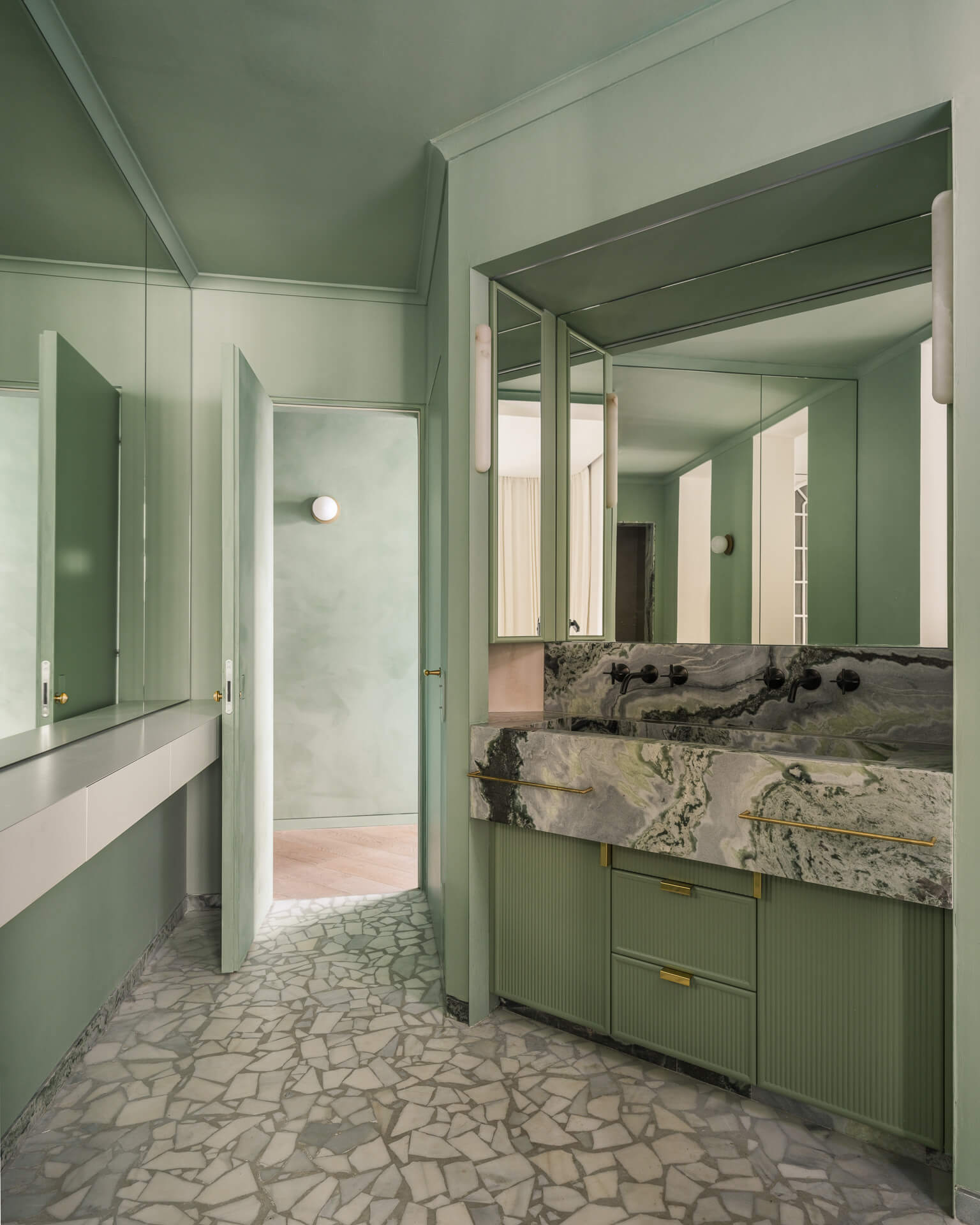 Green bathroom with mirrored cabinetry, heavily veined stone vanity, and mosaic stone floor.