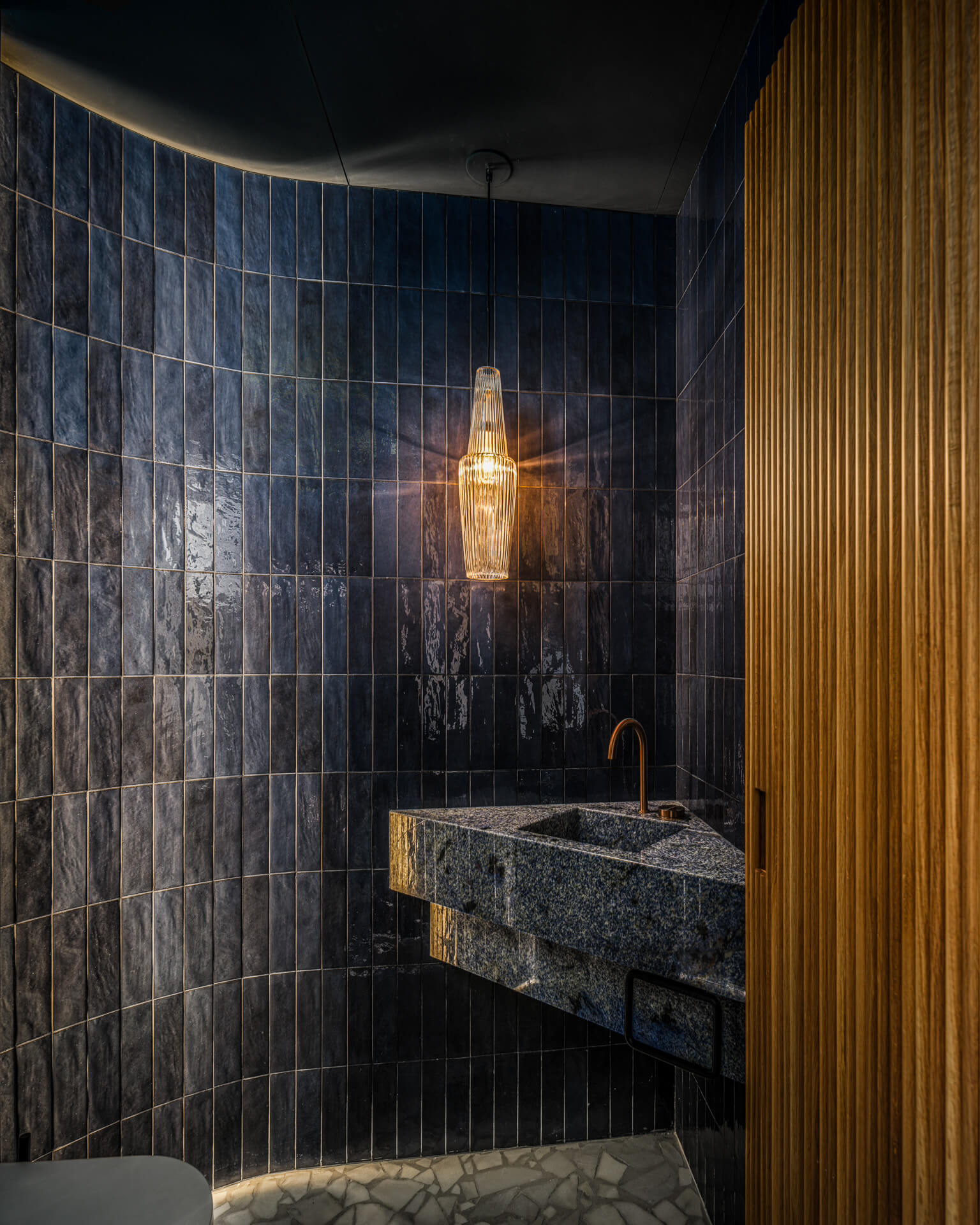 Moody powder room with deep blue tile walls, floating stone sink, pendant light, and vertical wood paneling.