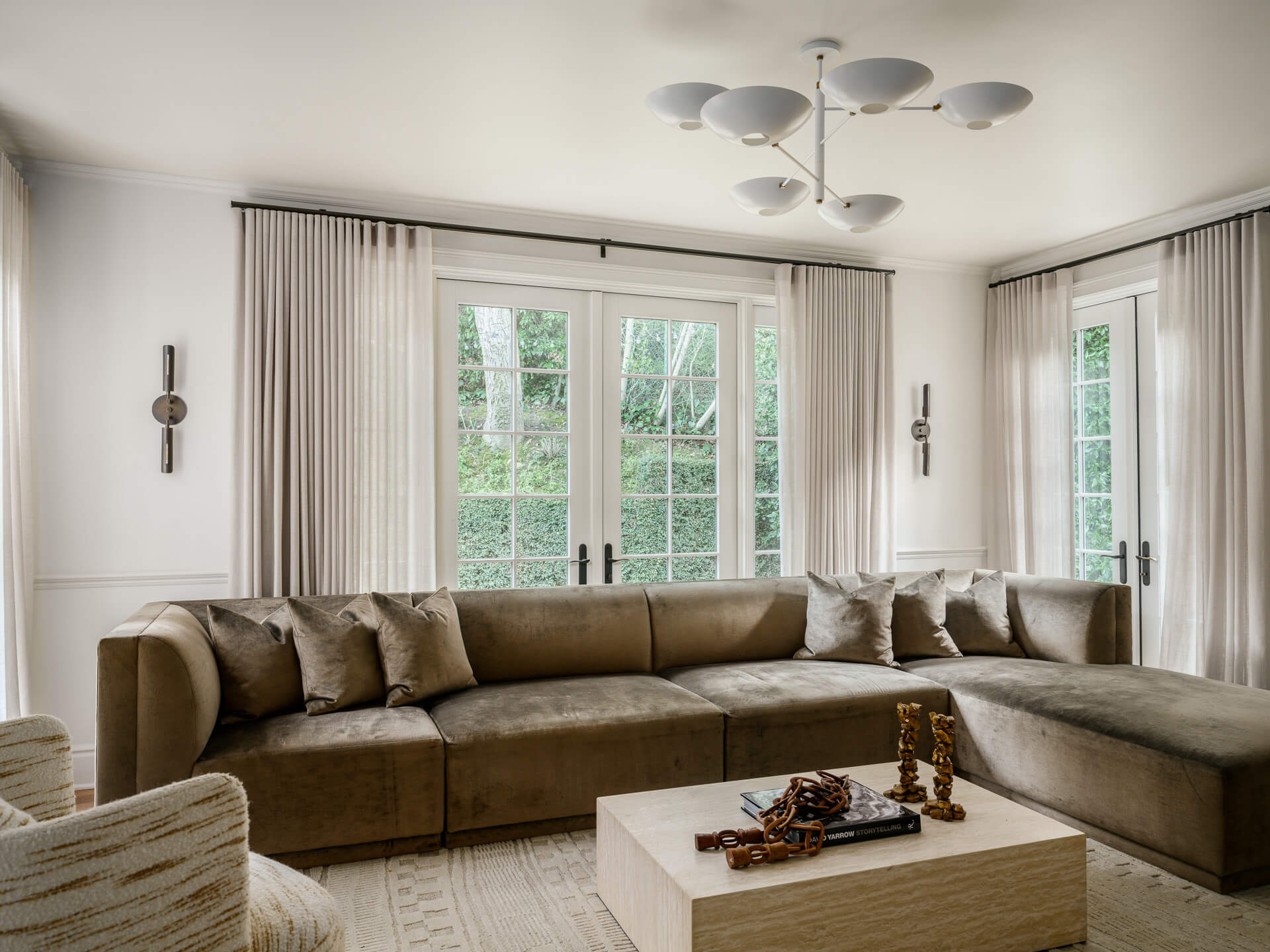 Family room with large taupe sectional, pale coffee table, tall curtained windows, and sculptural ceiling light.