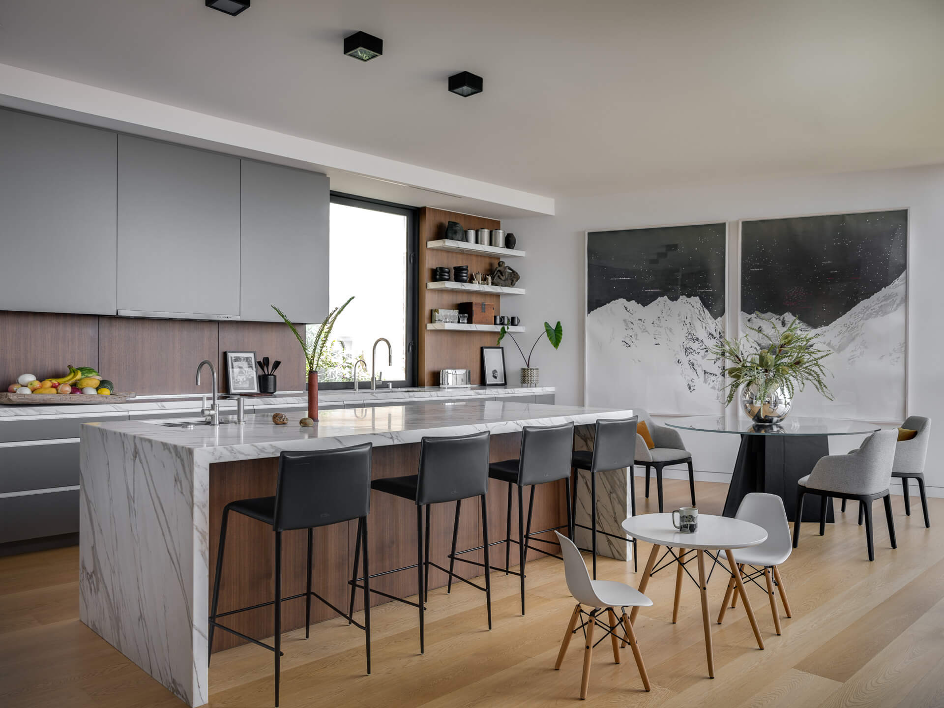 Contemporary kitchen with marble island, gray cabinetry, black stools, and large windows overlooking the city.