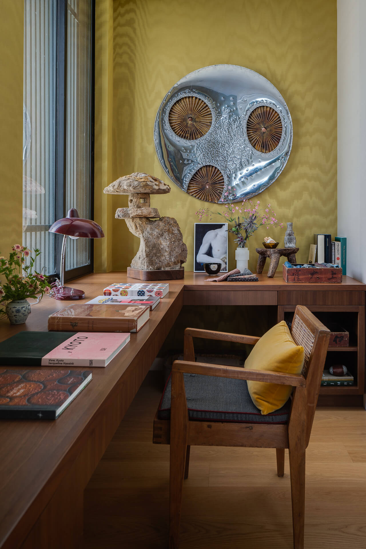 Warm home office with wood desk, yellow walls, sculptural artwork, and a large circular wall piece.