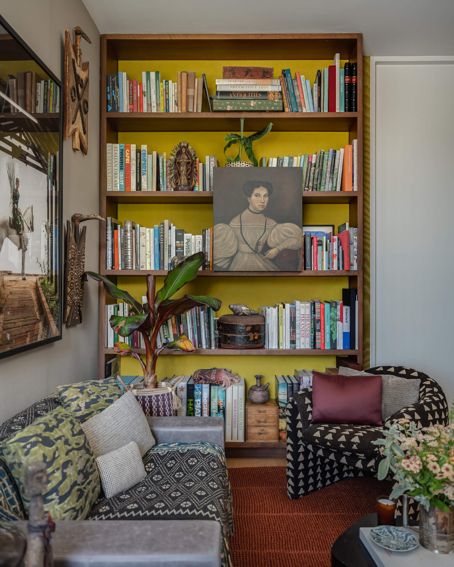 Cozy library with floor-to-ceiling bookshelves, patterned seating, colorful textiles, and framed portrait.