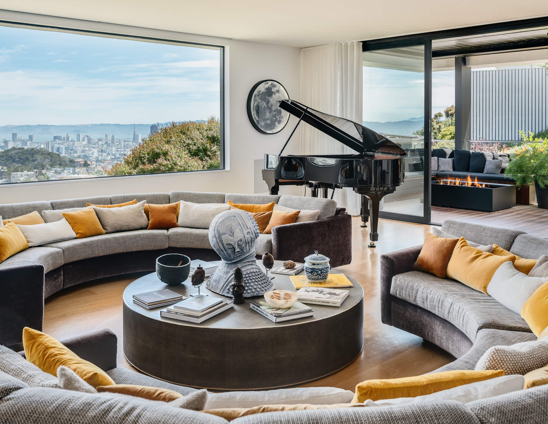 Curved living room with gray sectional, yellow pillows, grand piano, and expansive city views.