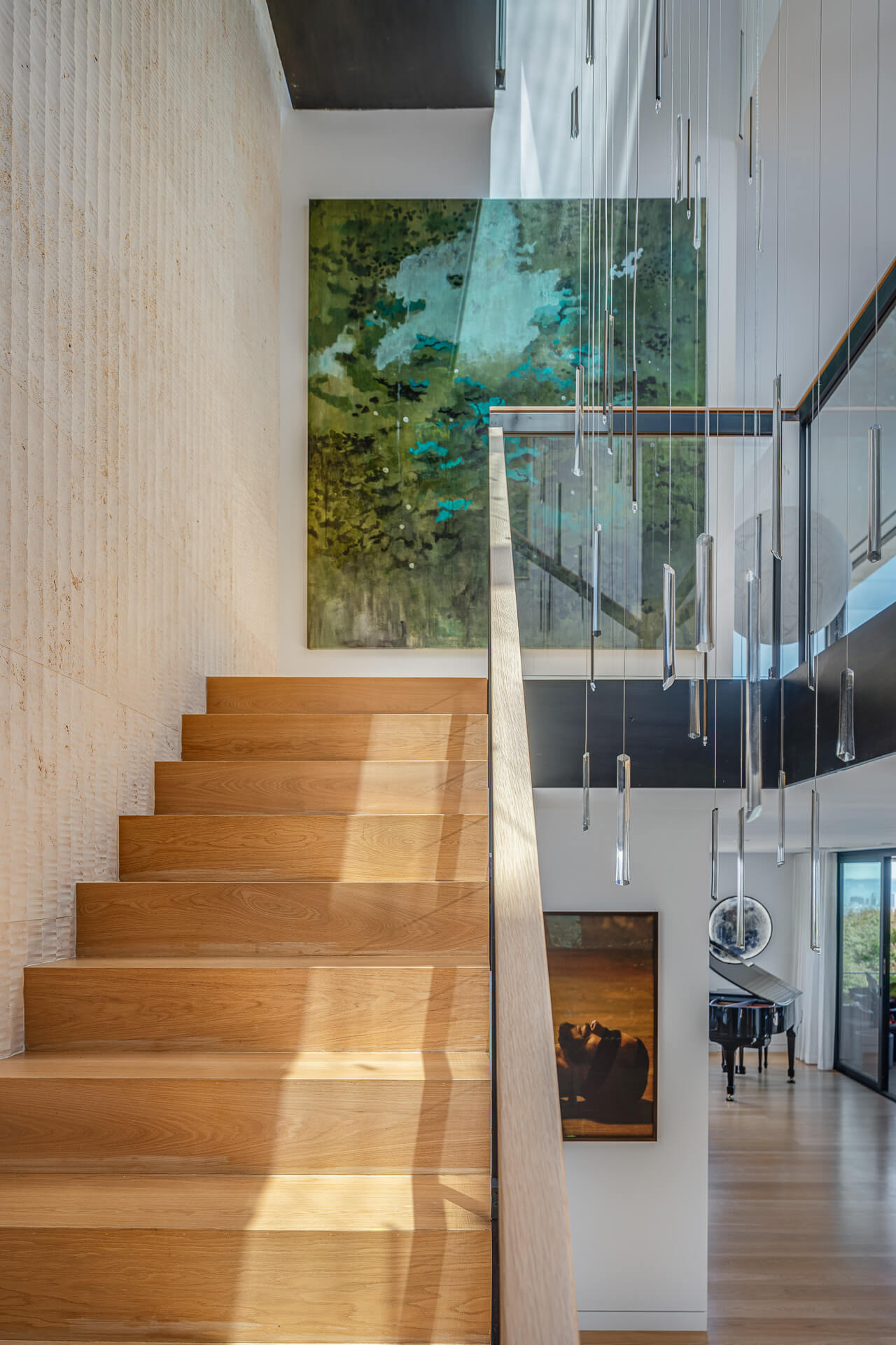 Floating wood staircase beside a glass wall and hanging light installation in a double-height interior.
