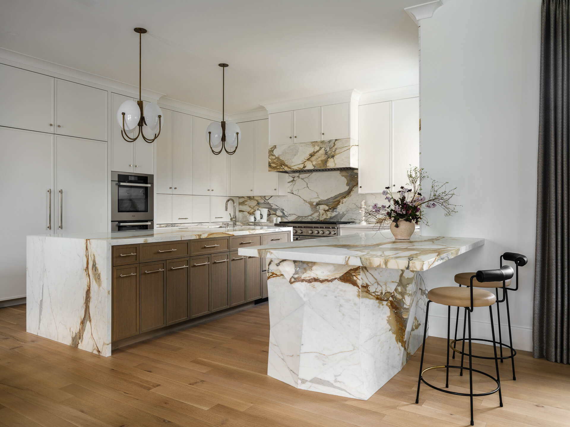 White kitchen with dramatic veined marble island and backsplash, brass accents, and counter stools.