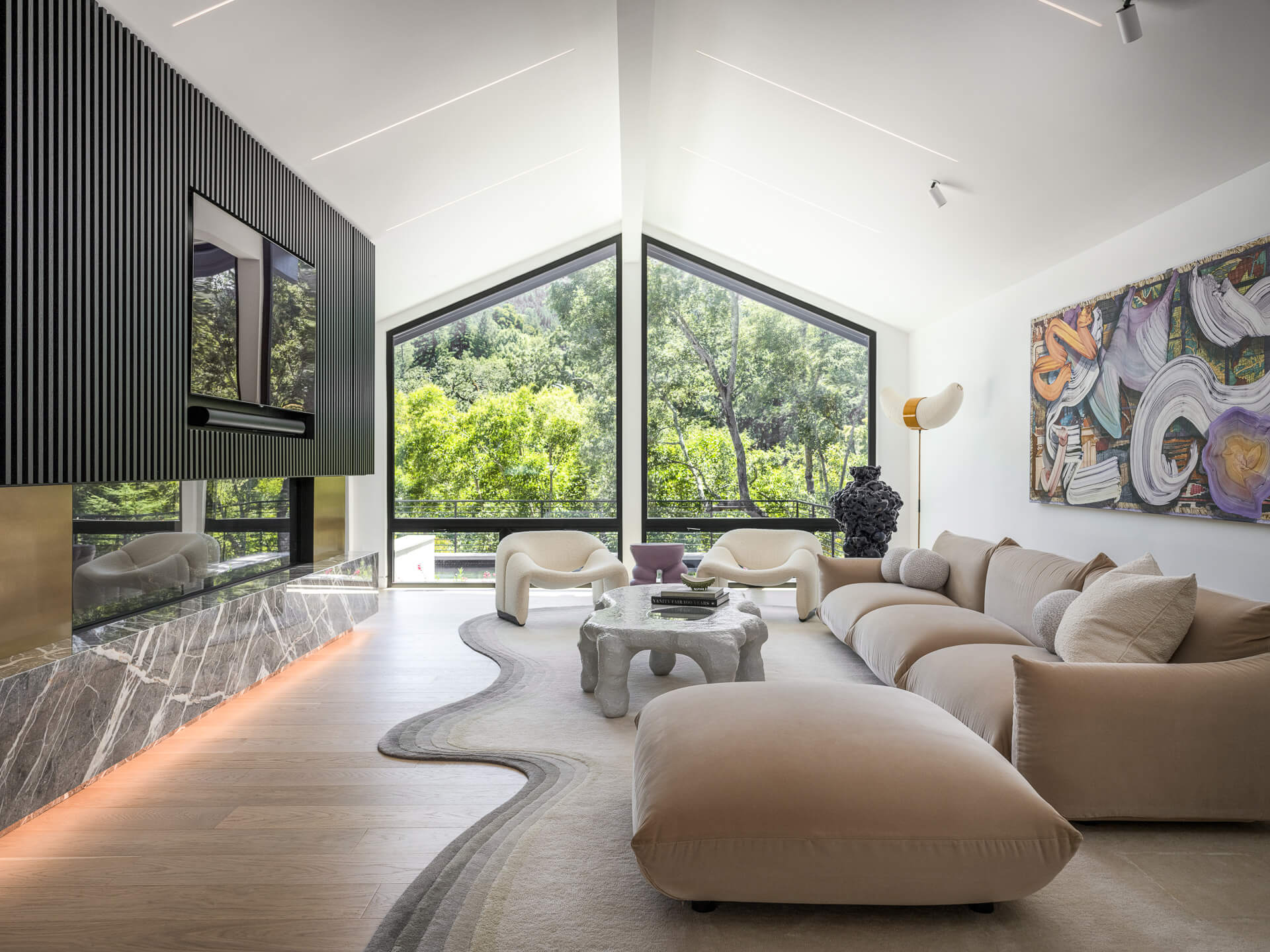 Sculptural living room with curved cream sectional, abstract artwork, marble fireplace, and floor-to-ceiling windows.