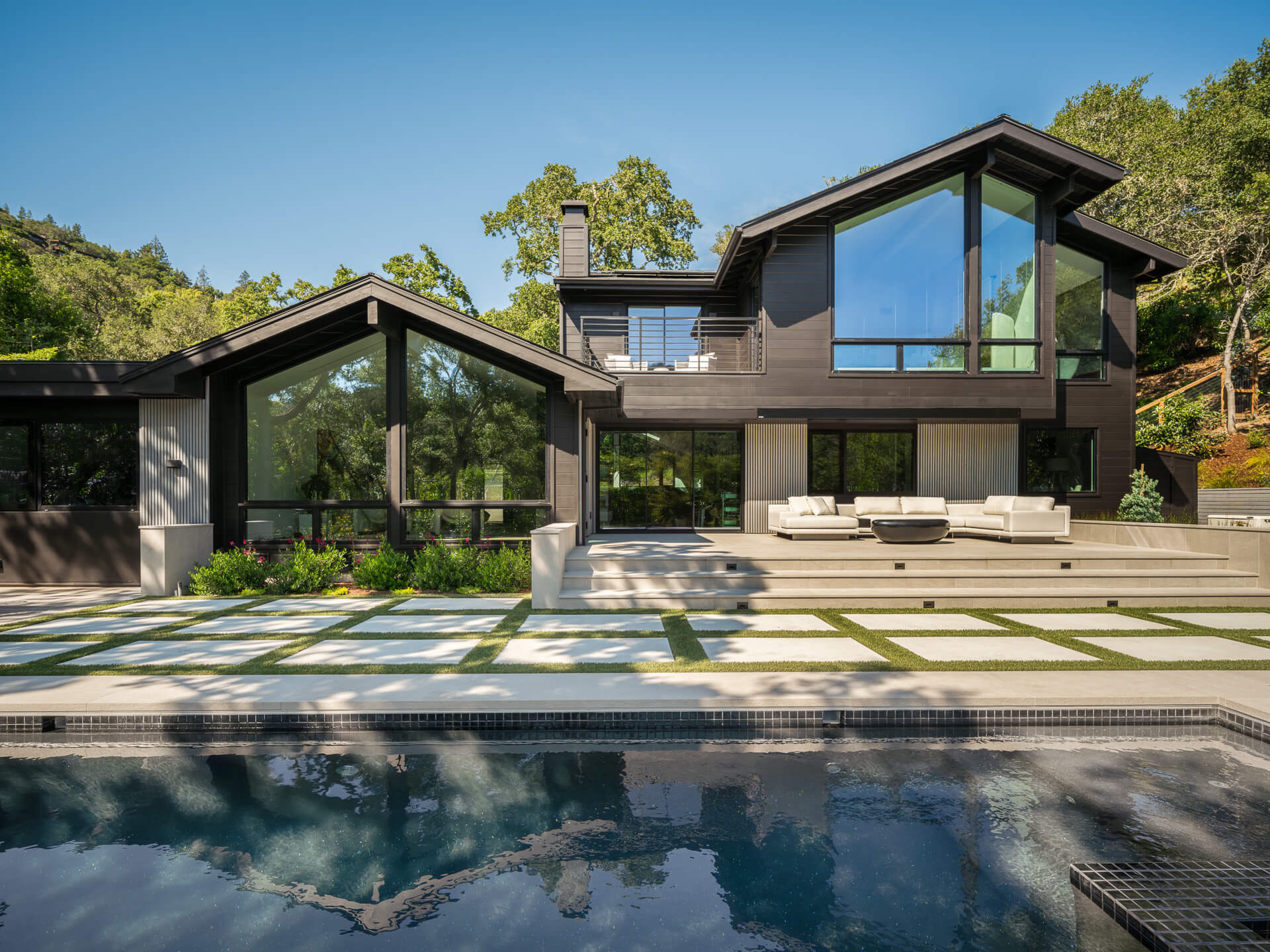 Contemporary hillside home with dark exterior, large windows, landscaped terrace, and swimming pool.