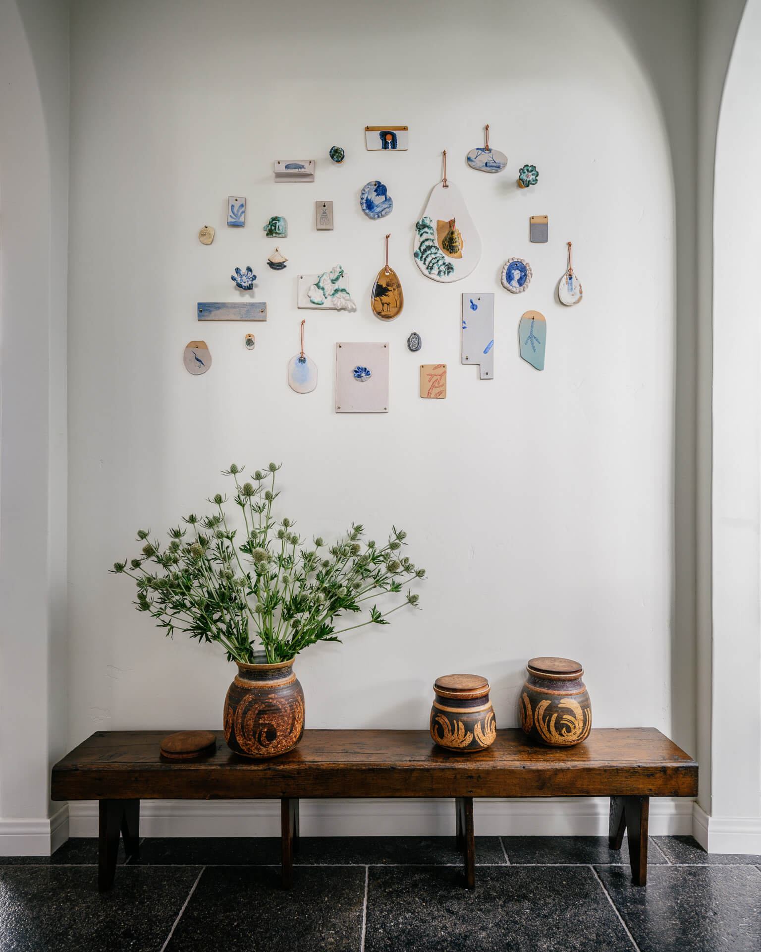 Wood bench beneath a collection of small artworks and ceramics in an arched alcove