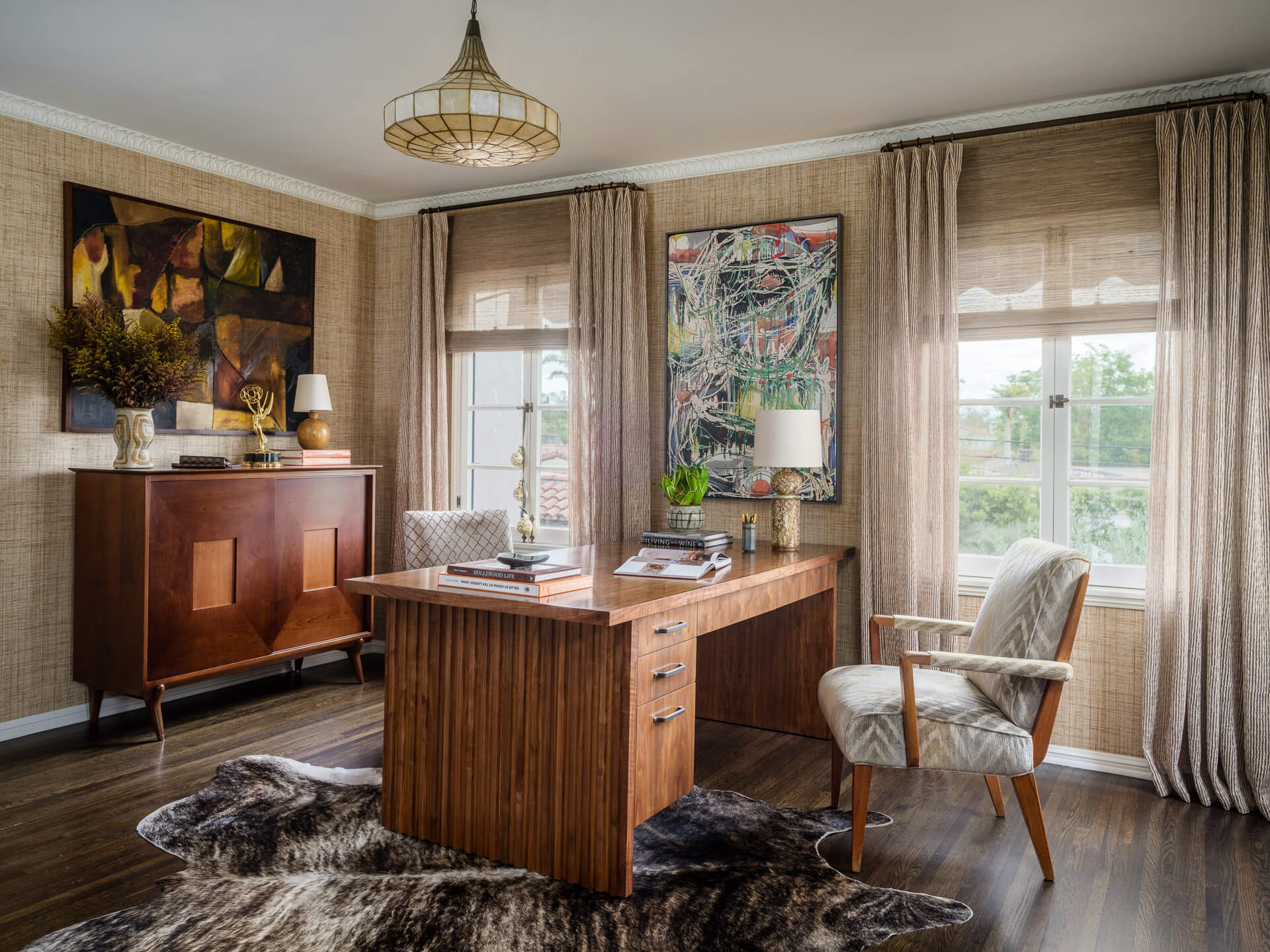 Warm wood home office with vintage furniture, layered artwork and textured window treatments
