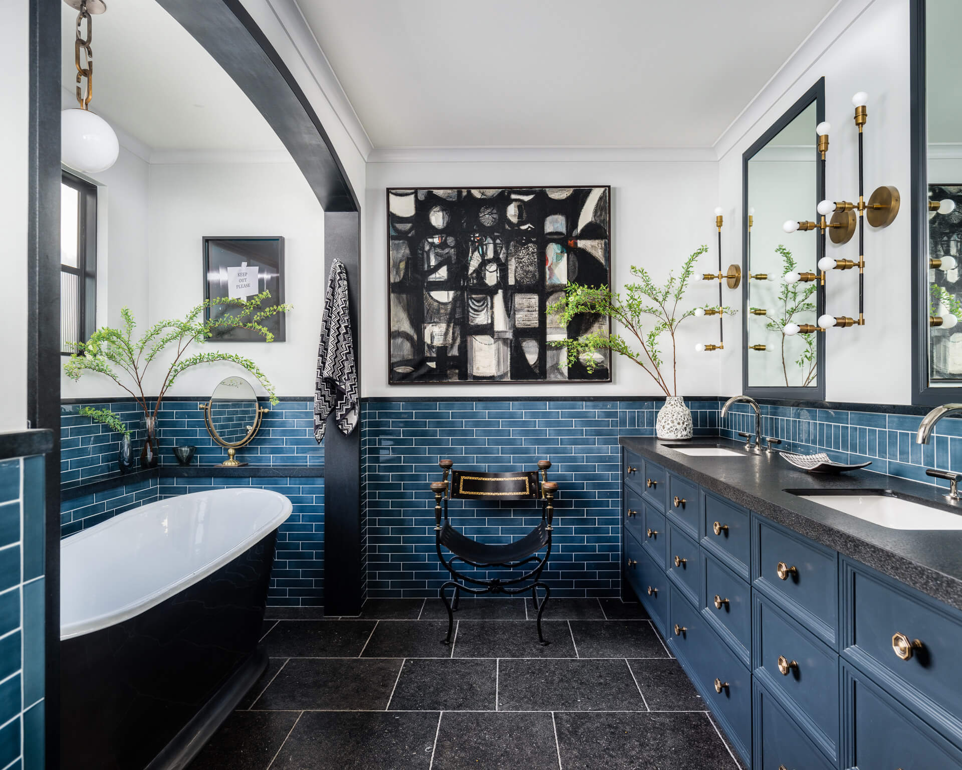 Blue-tiled bathroom with freestanding tub, double vanity and brass lighting