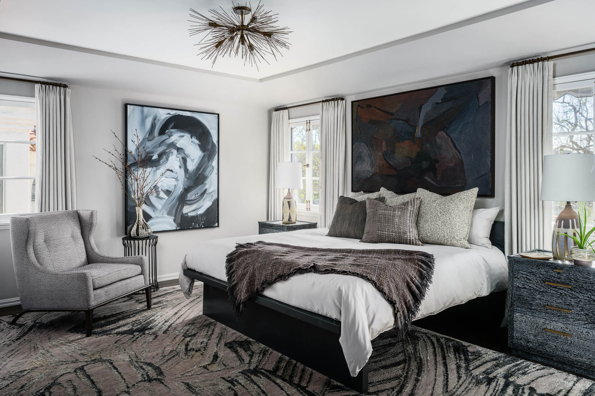 Monochromatic bedroom with dark upholstered bed, abstract artwork and patterned rug