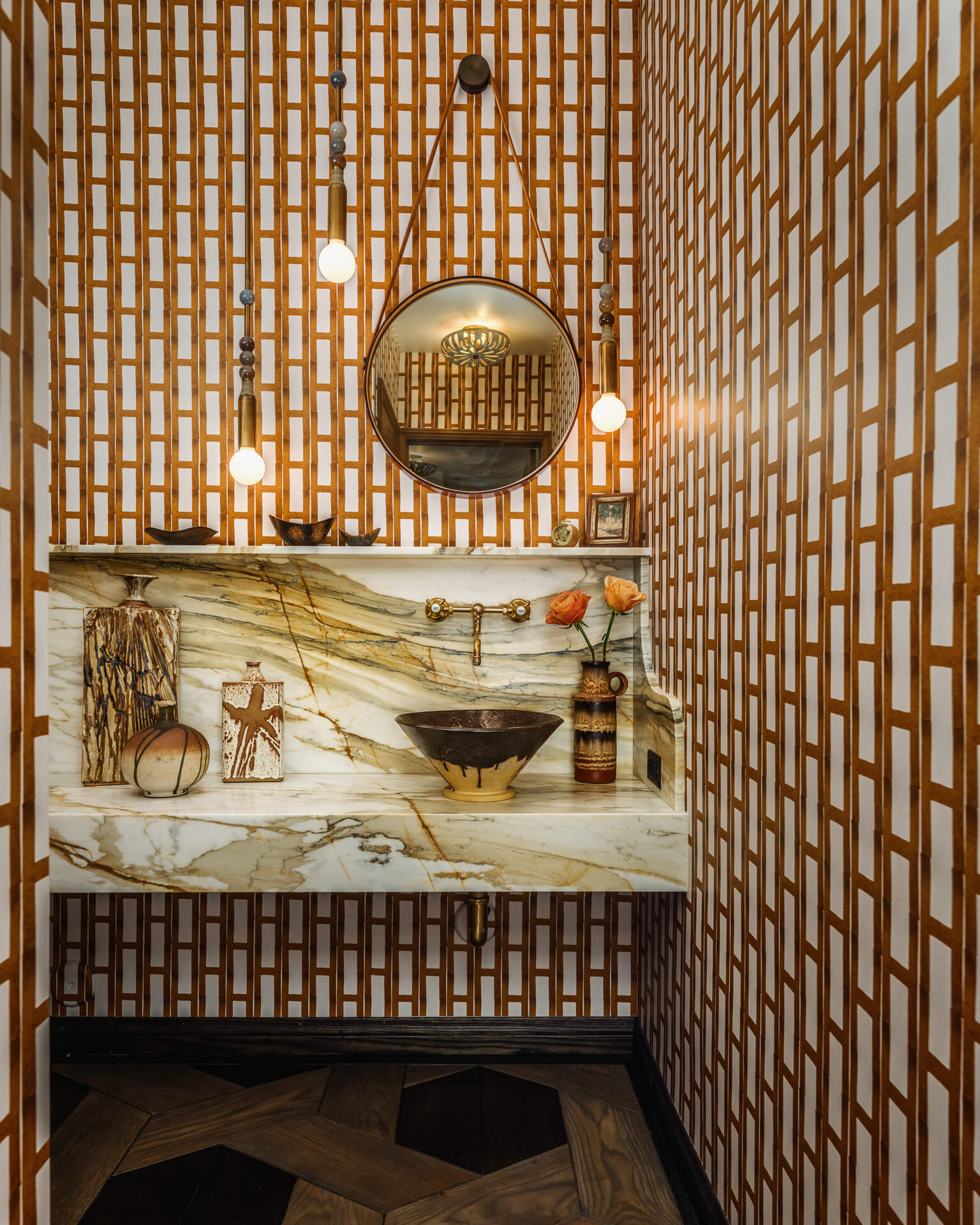 Powder room with geometric brown wallpaper, marble sink and round brass mirror