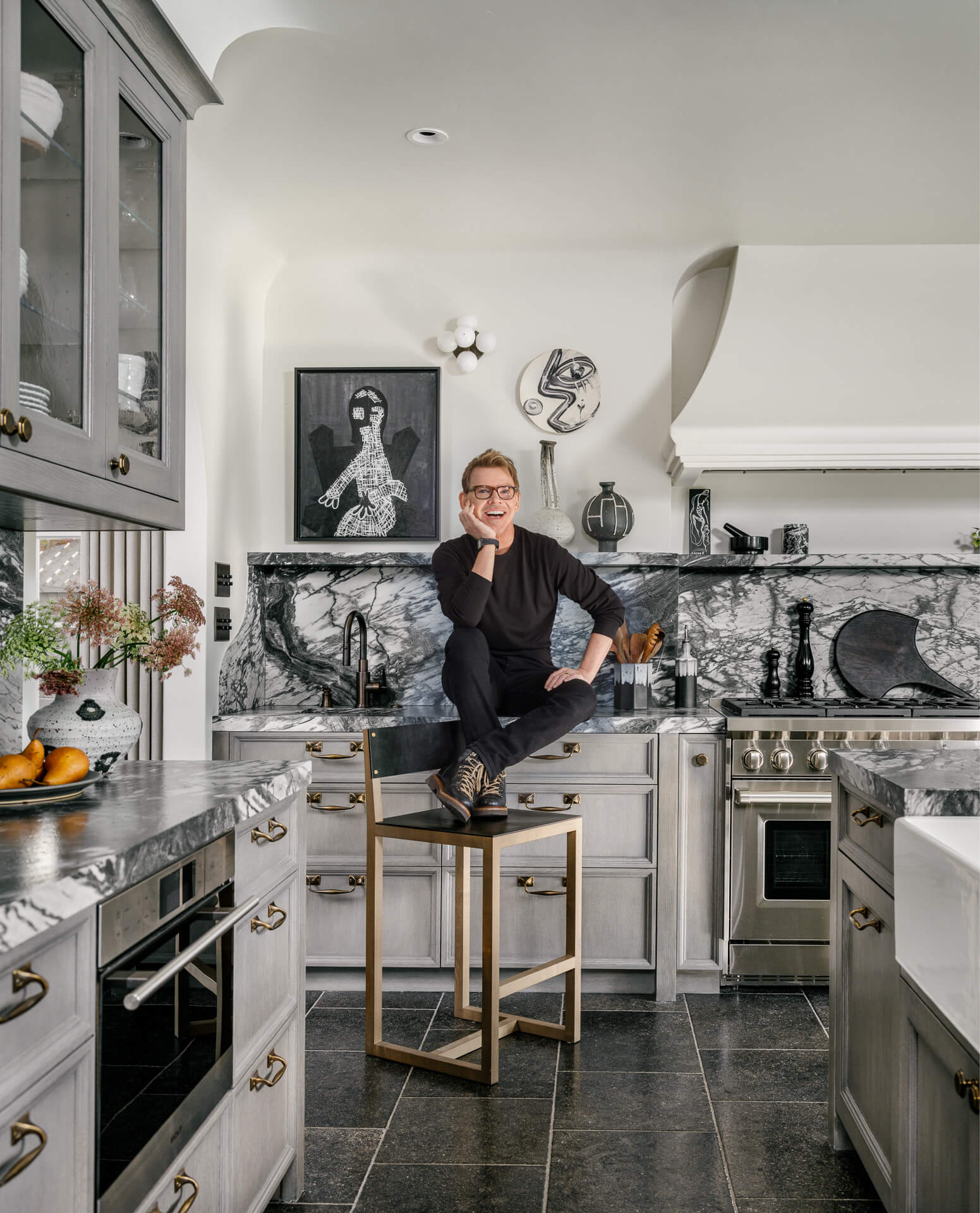 Interior designer Jeff Andrews seated in his black-and-white marble kitchen with brass accents