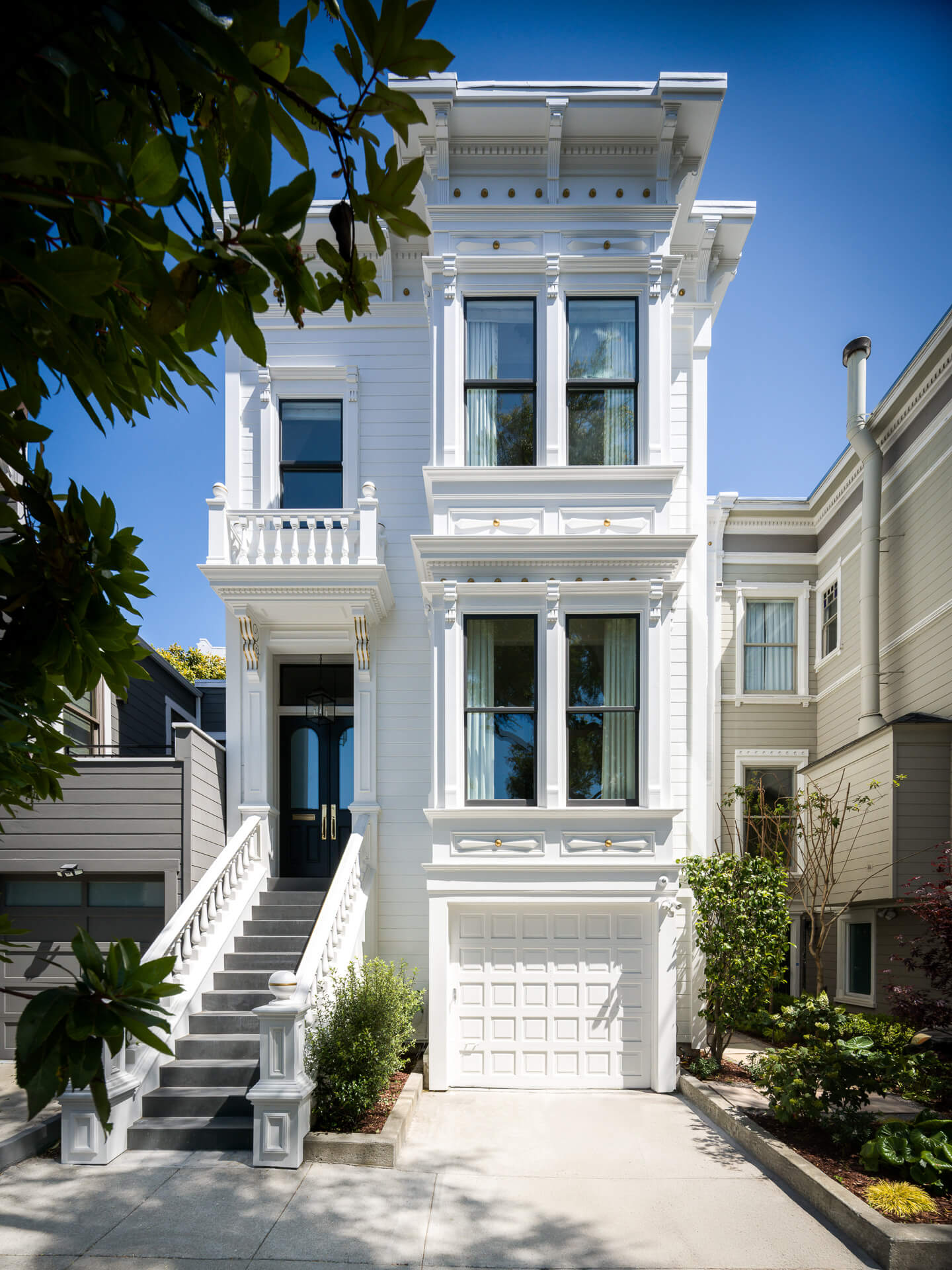 Ornate white Victorian facade with tall windows, front steps, and an integrated garage.